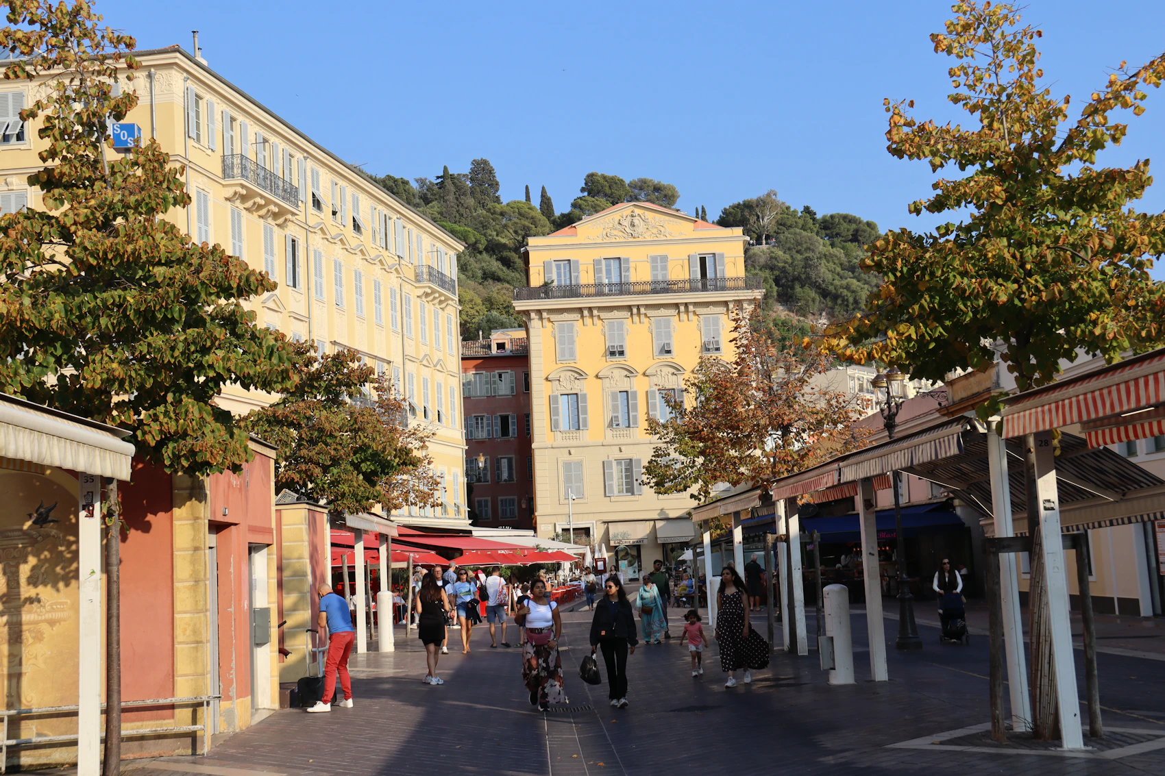 People strolling between striped awnings at Cours Saleya market in Nice