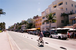 Person cycles down a sunny street lined with buildings.