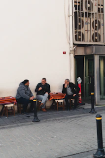 Three men sitting at tables outside a building.