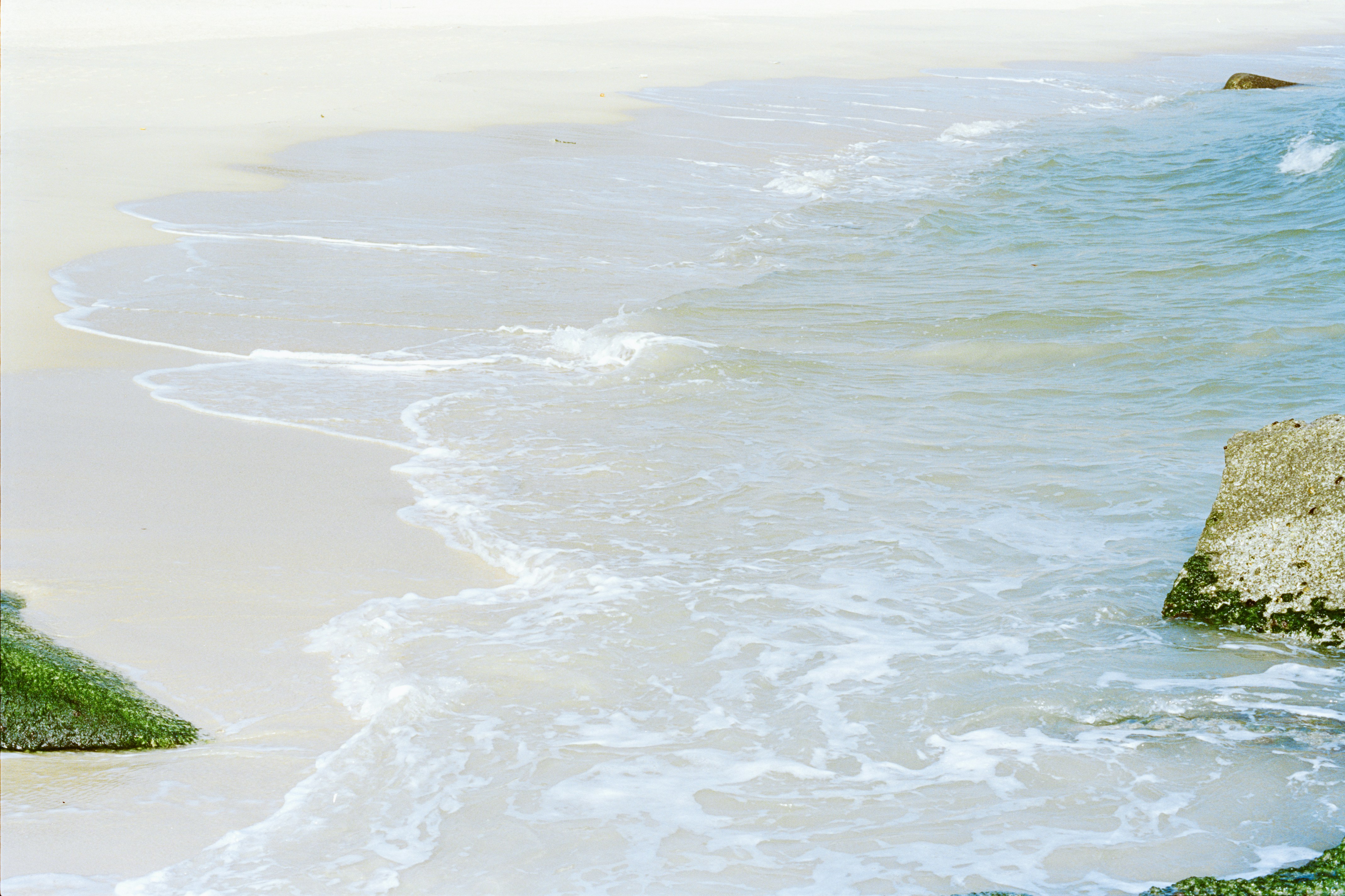 穏やかな波が岩のある砂浜を洗い流します。