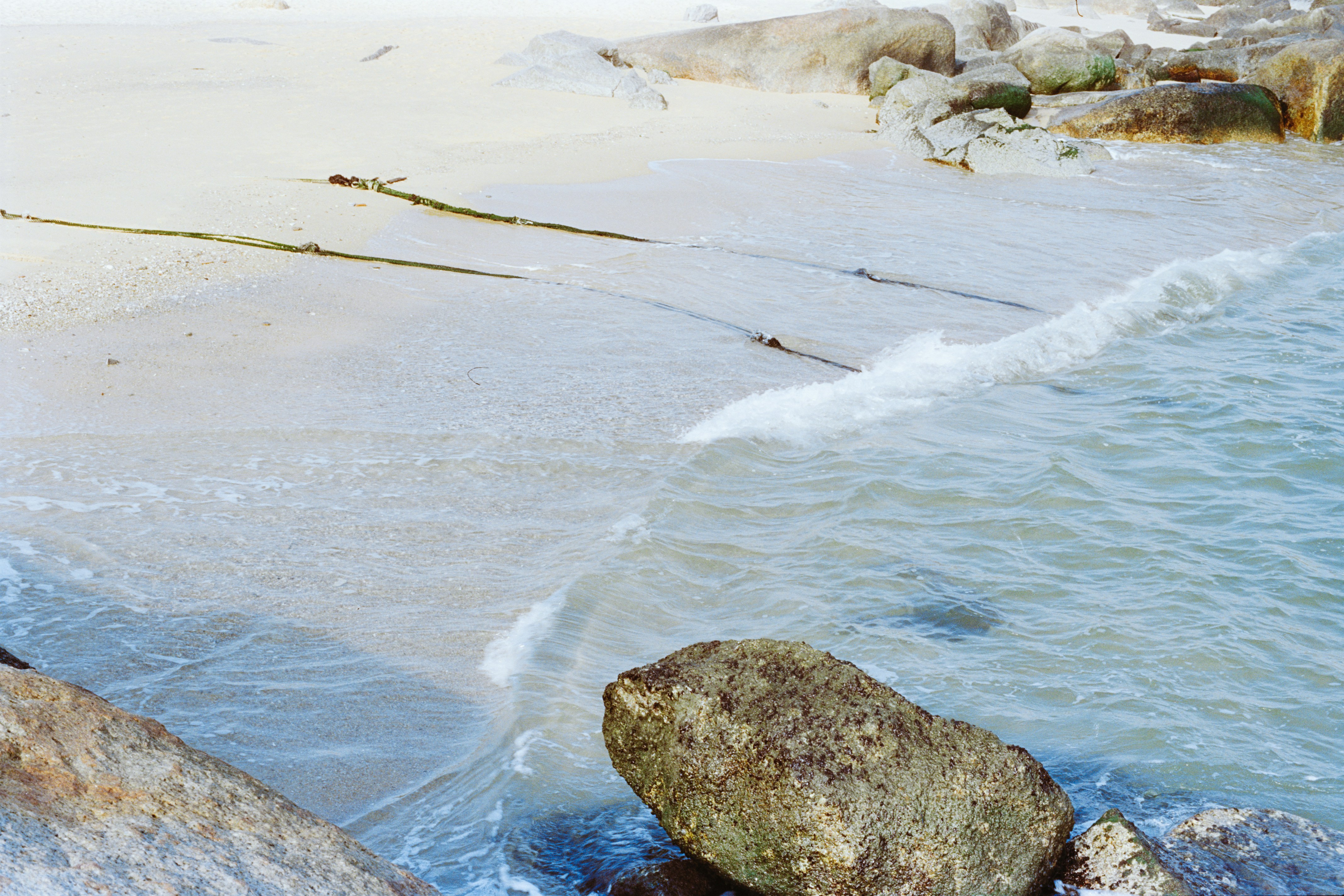 波が砂浜に優しく打ち寄せ、岩が散らばっている。
