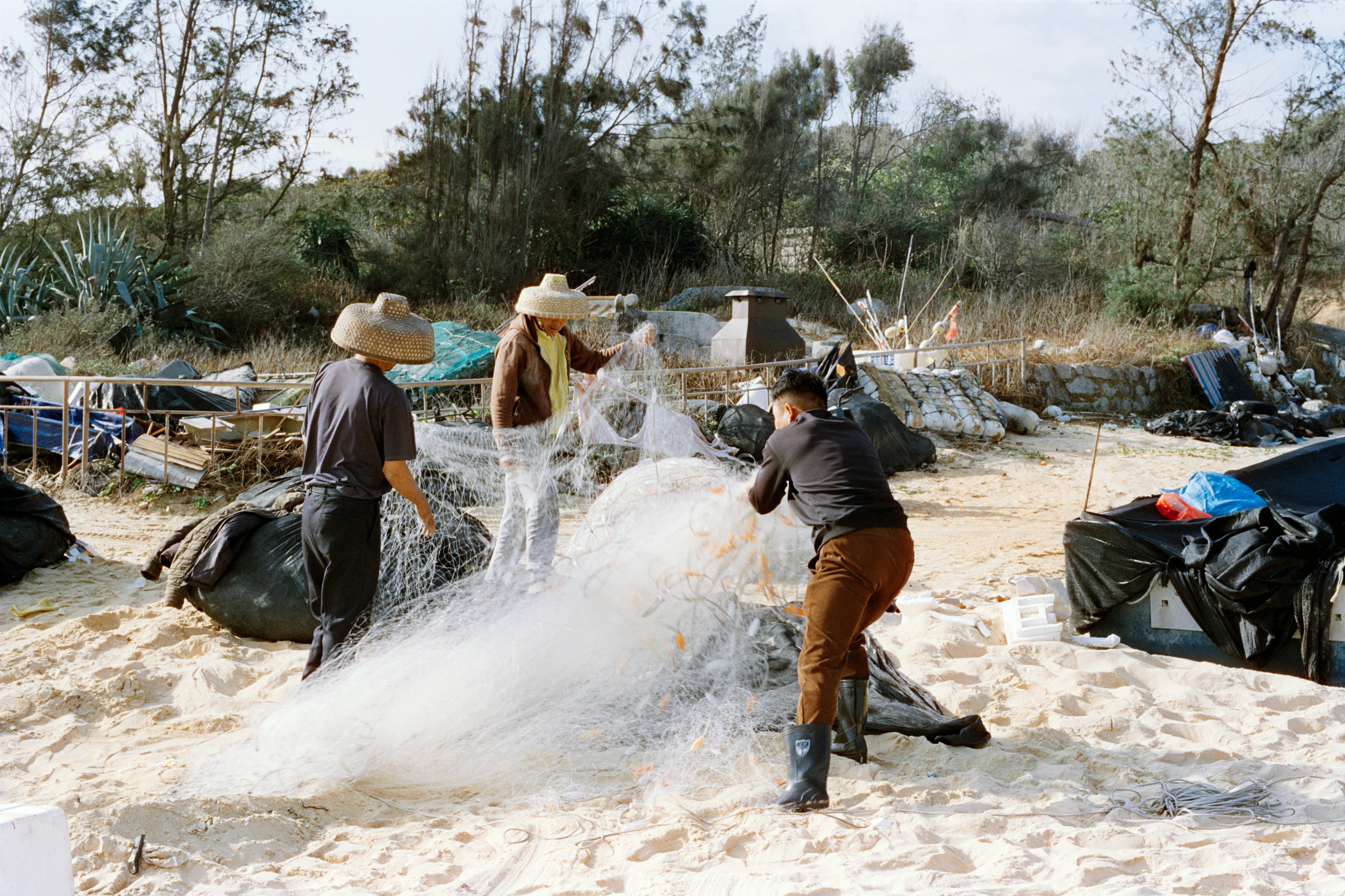 浜辺で3人が漁網をほどいている。