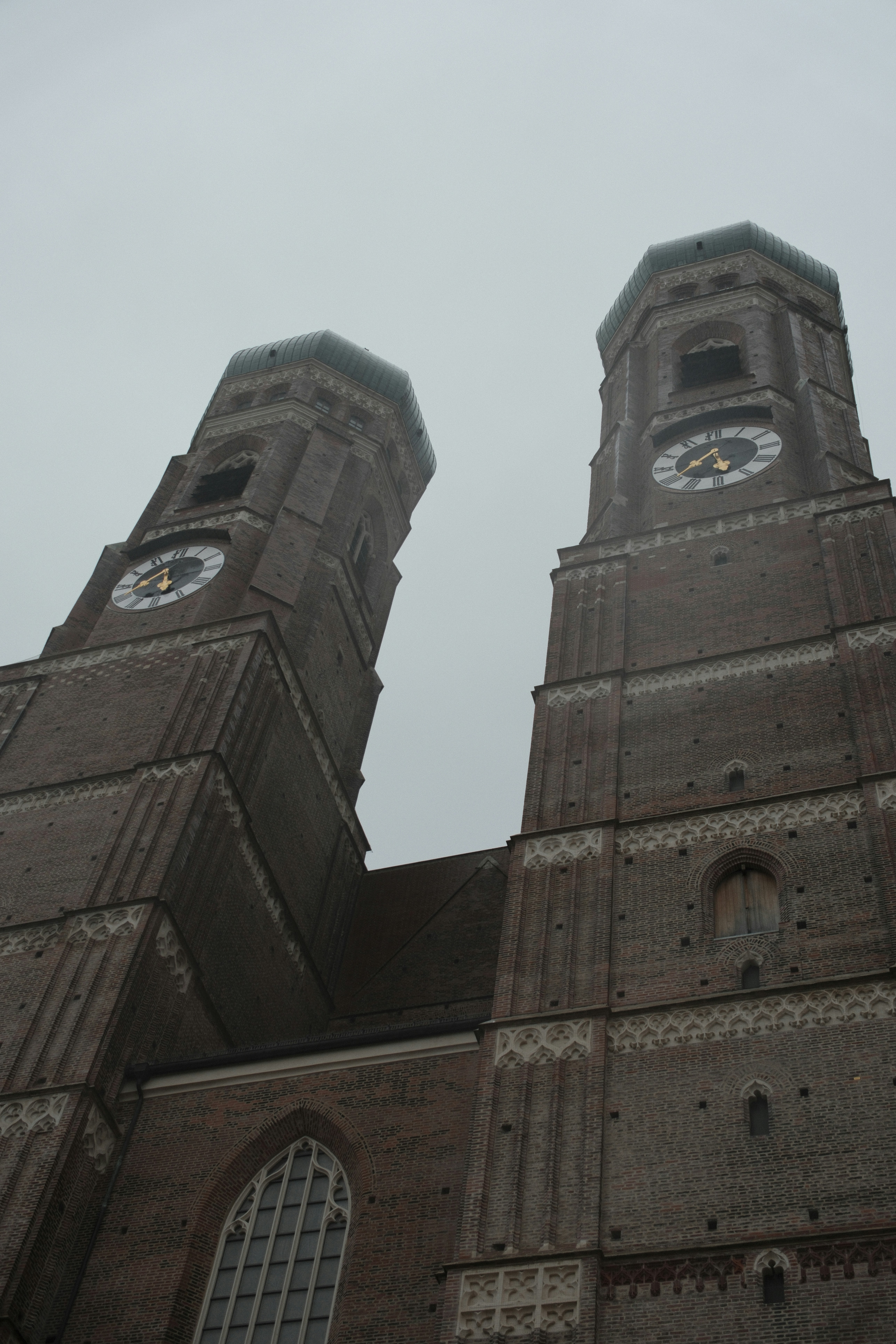 Two tall church towers with clocks against a cloudy sky.