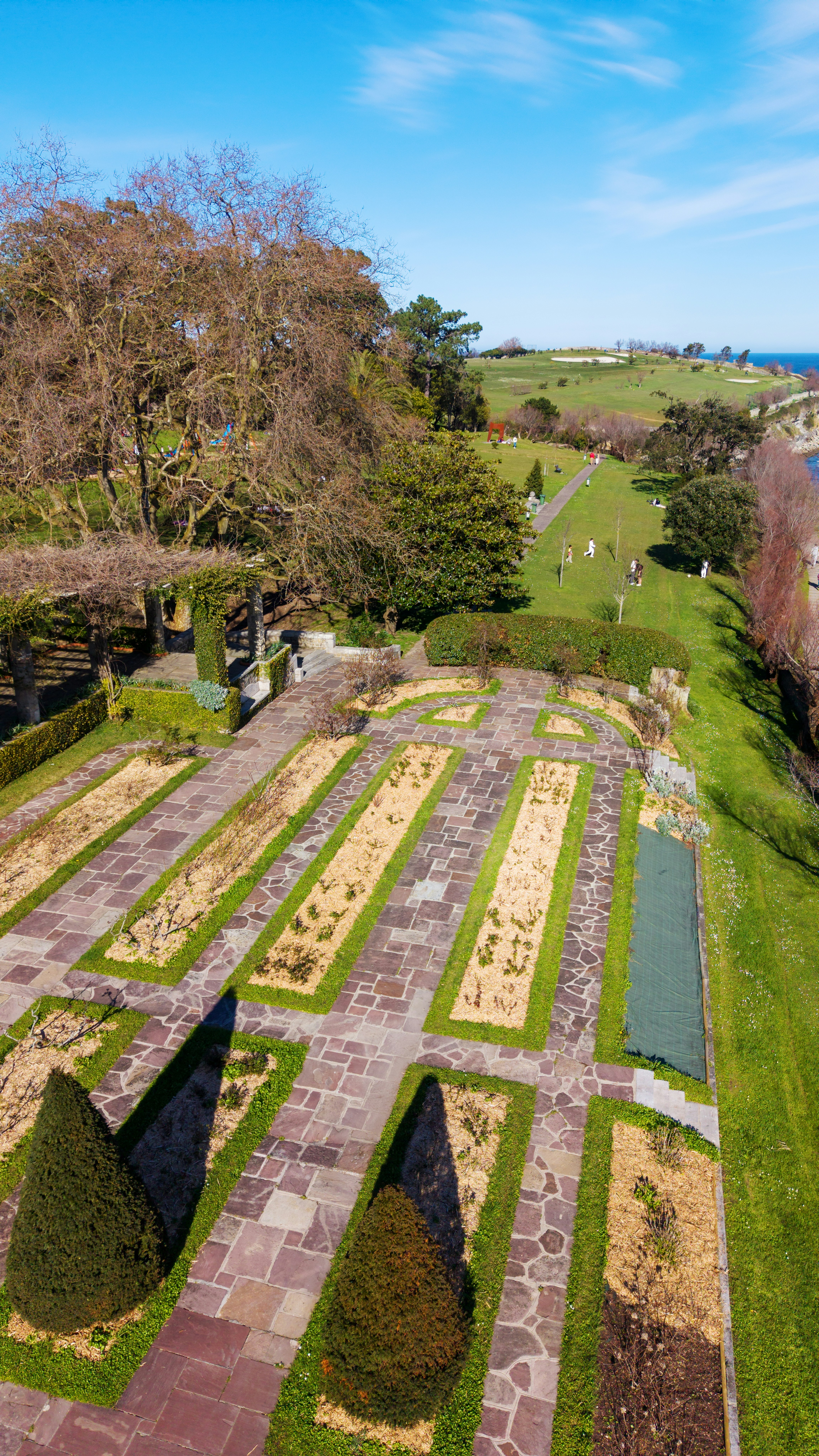 Formal garden beds with manicured trees and ocean view.