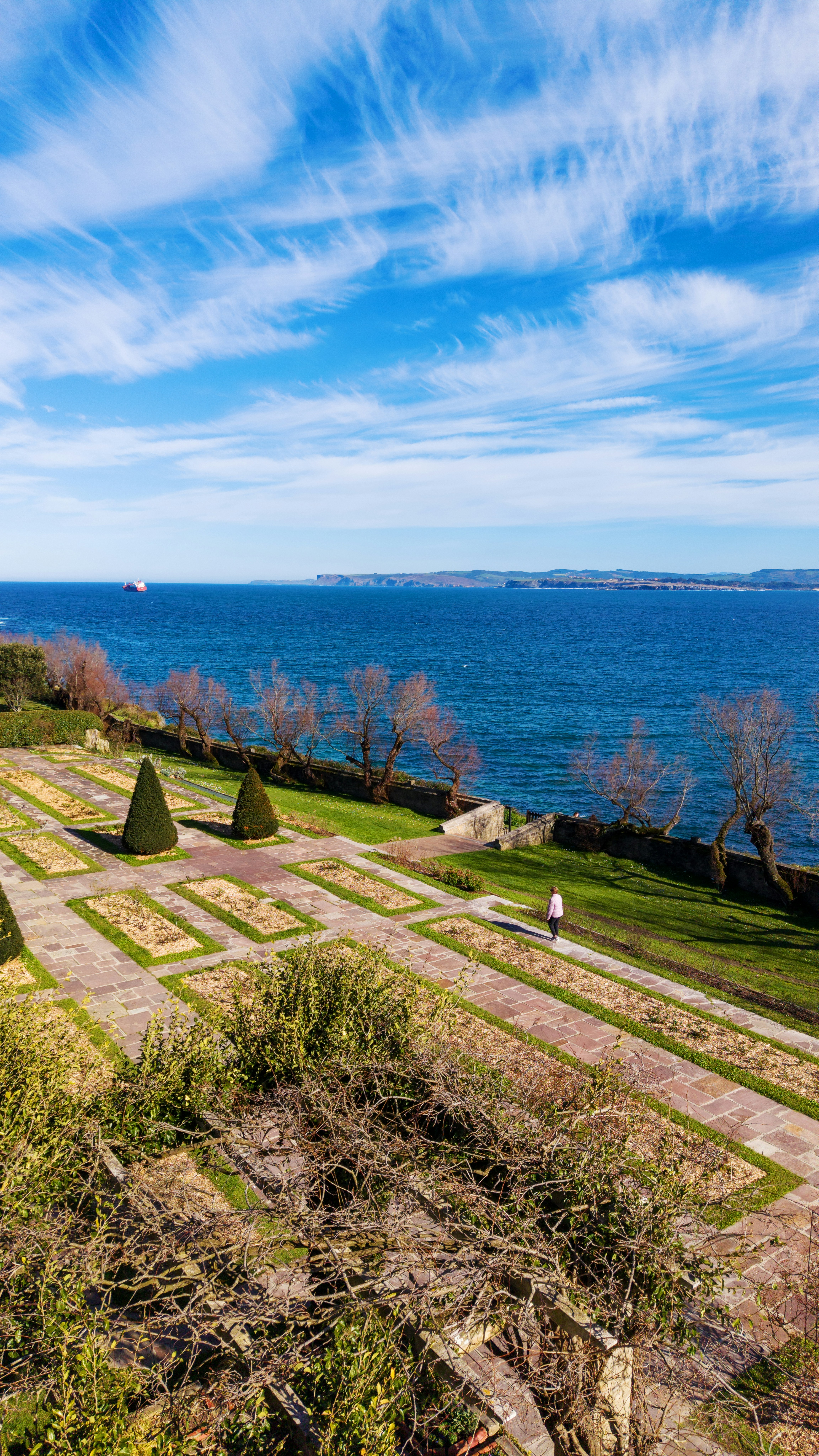 A person walks through a manicured garden by the sea.