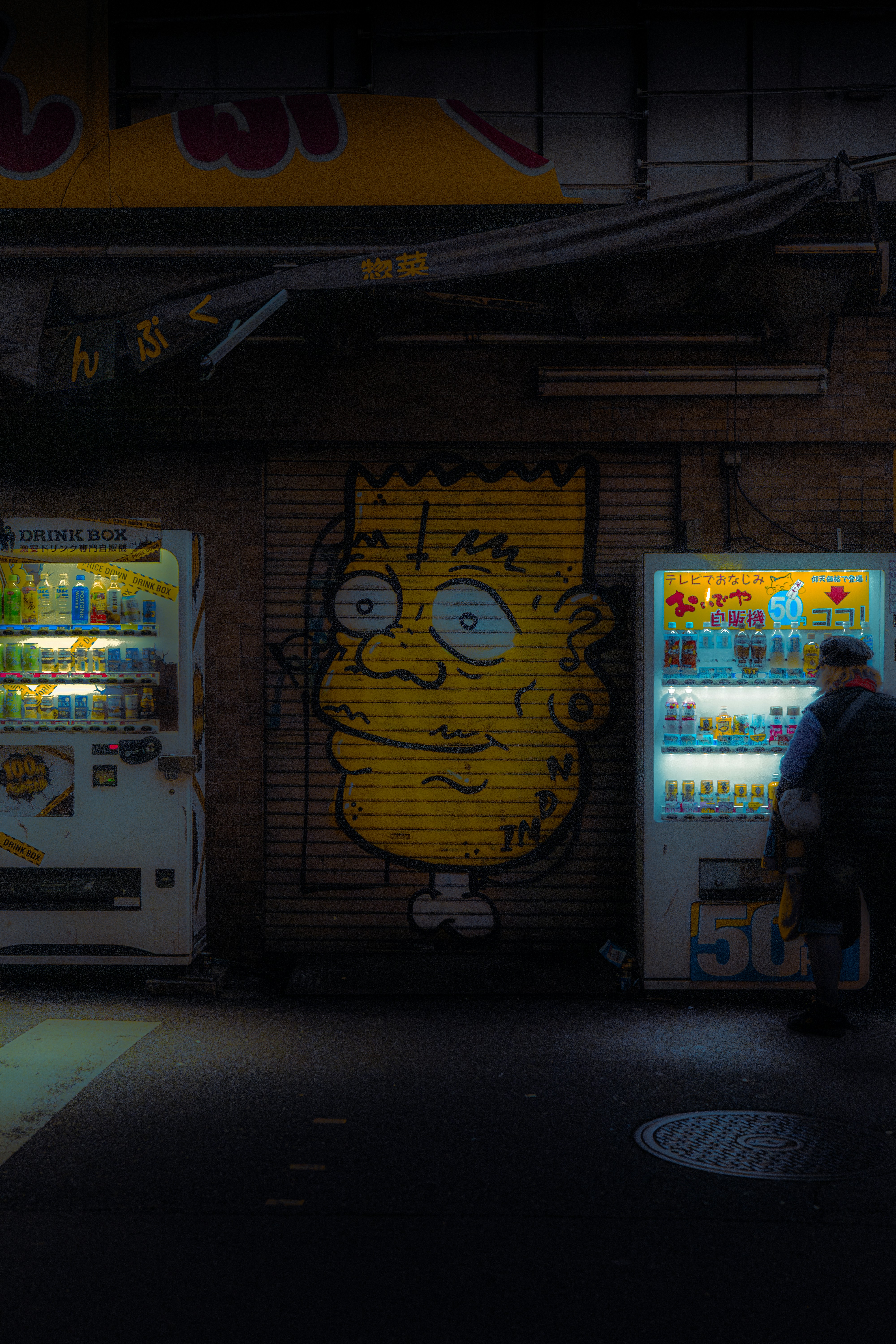 Bart simpson graffiti between two vending machines at night