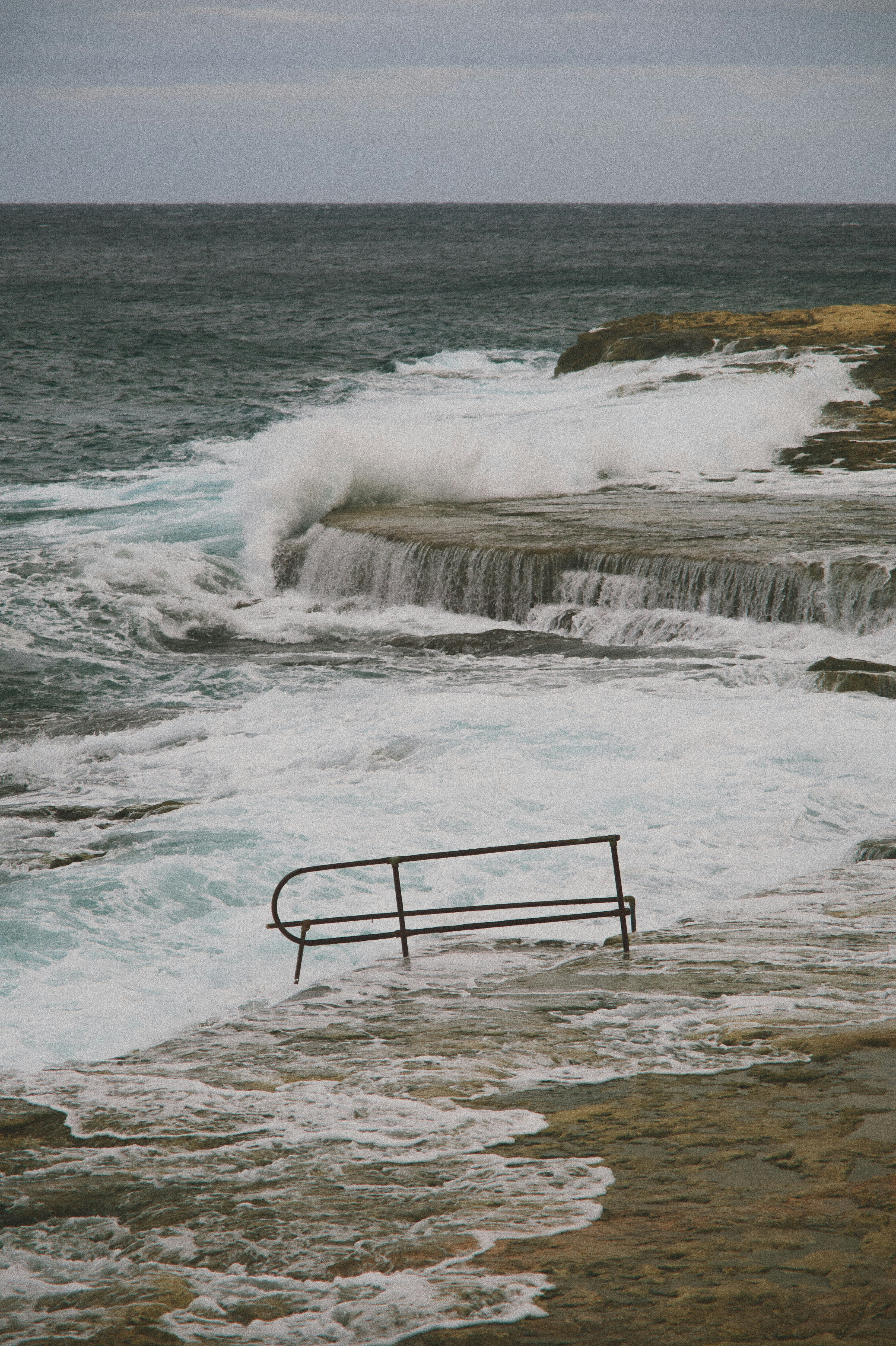 Waves crashing on rocky shore with metal railing