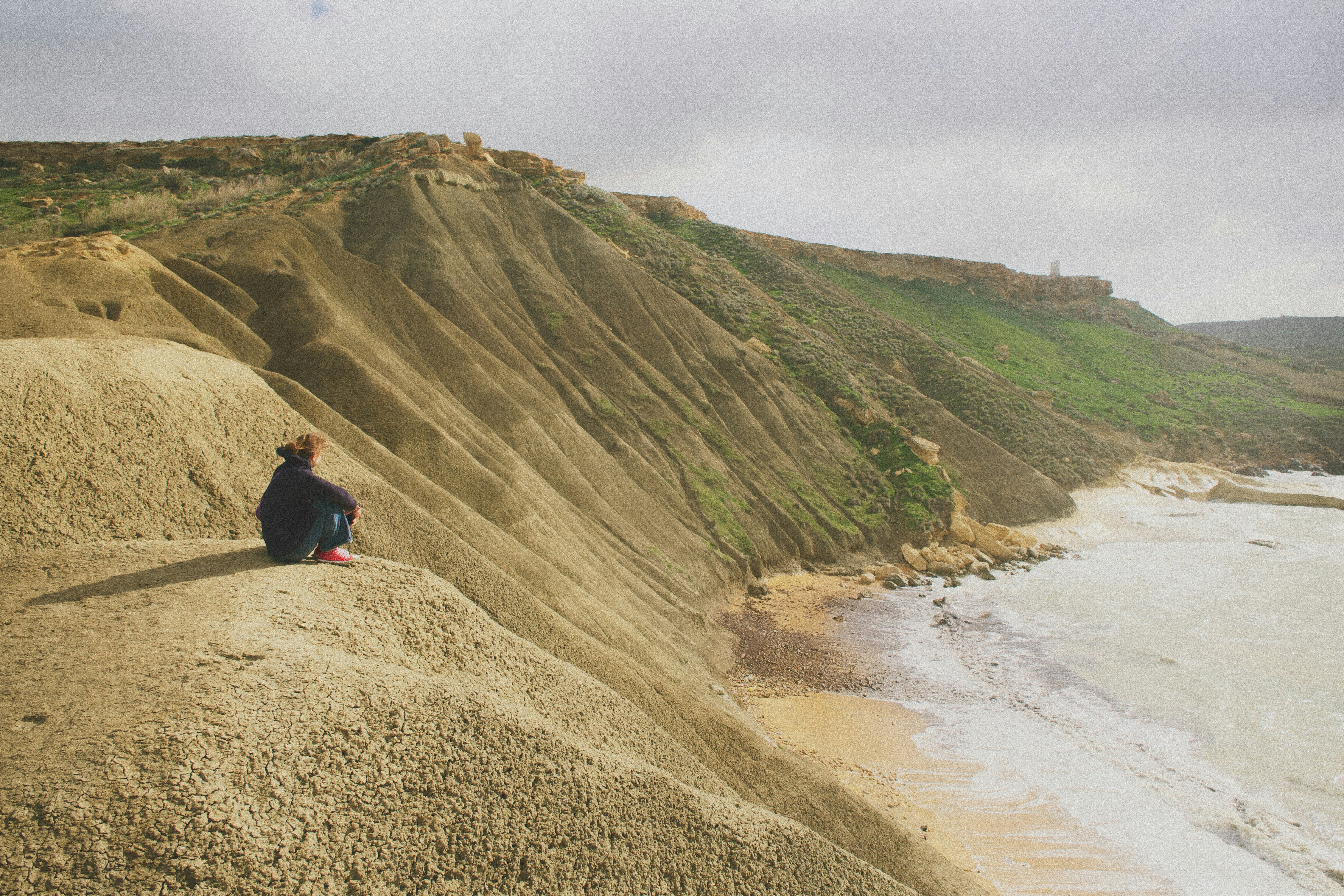 Person sitting on a cliff overlooking the ocean
