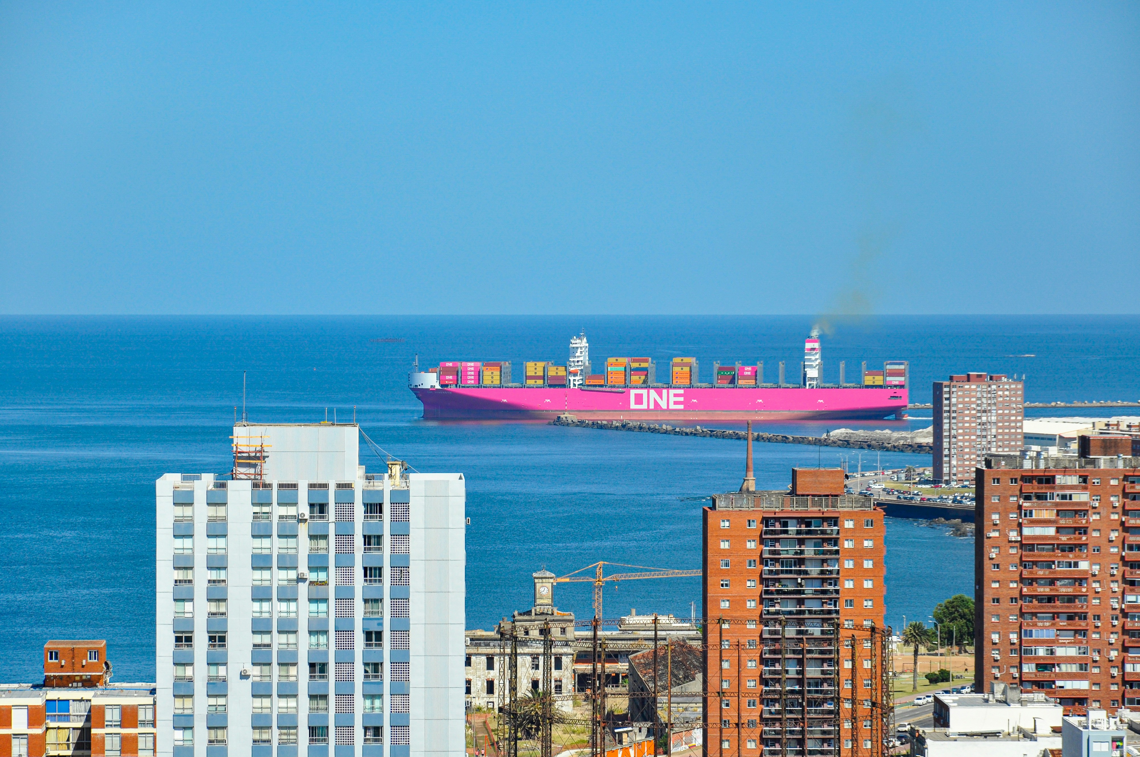 Grande navio cargueiro rosa navegando no oceano azul perto da cidade.