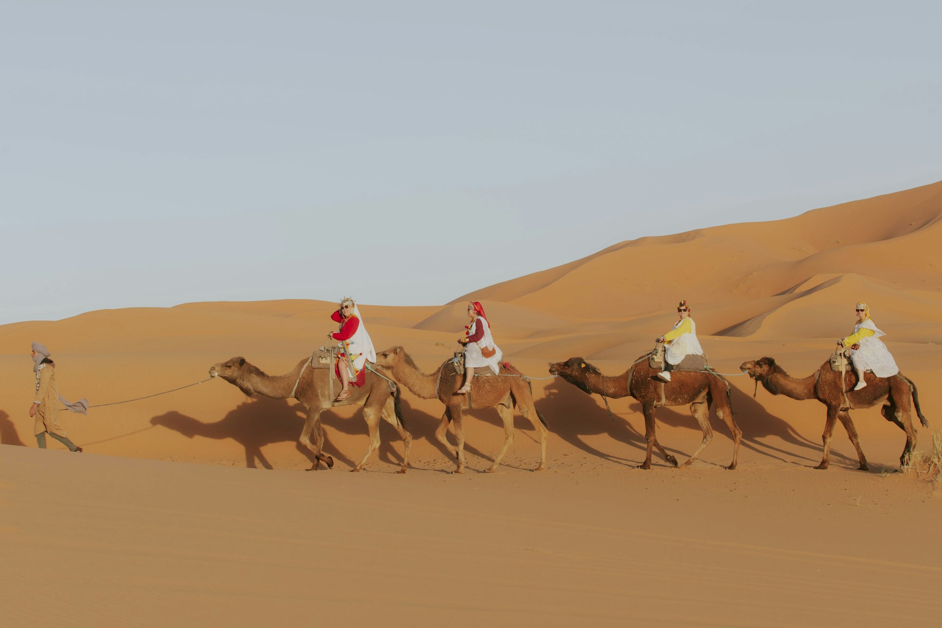 Caravan of camels crossing a vast desert at sunset
