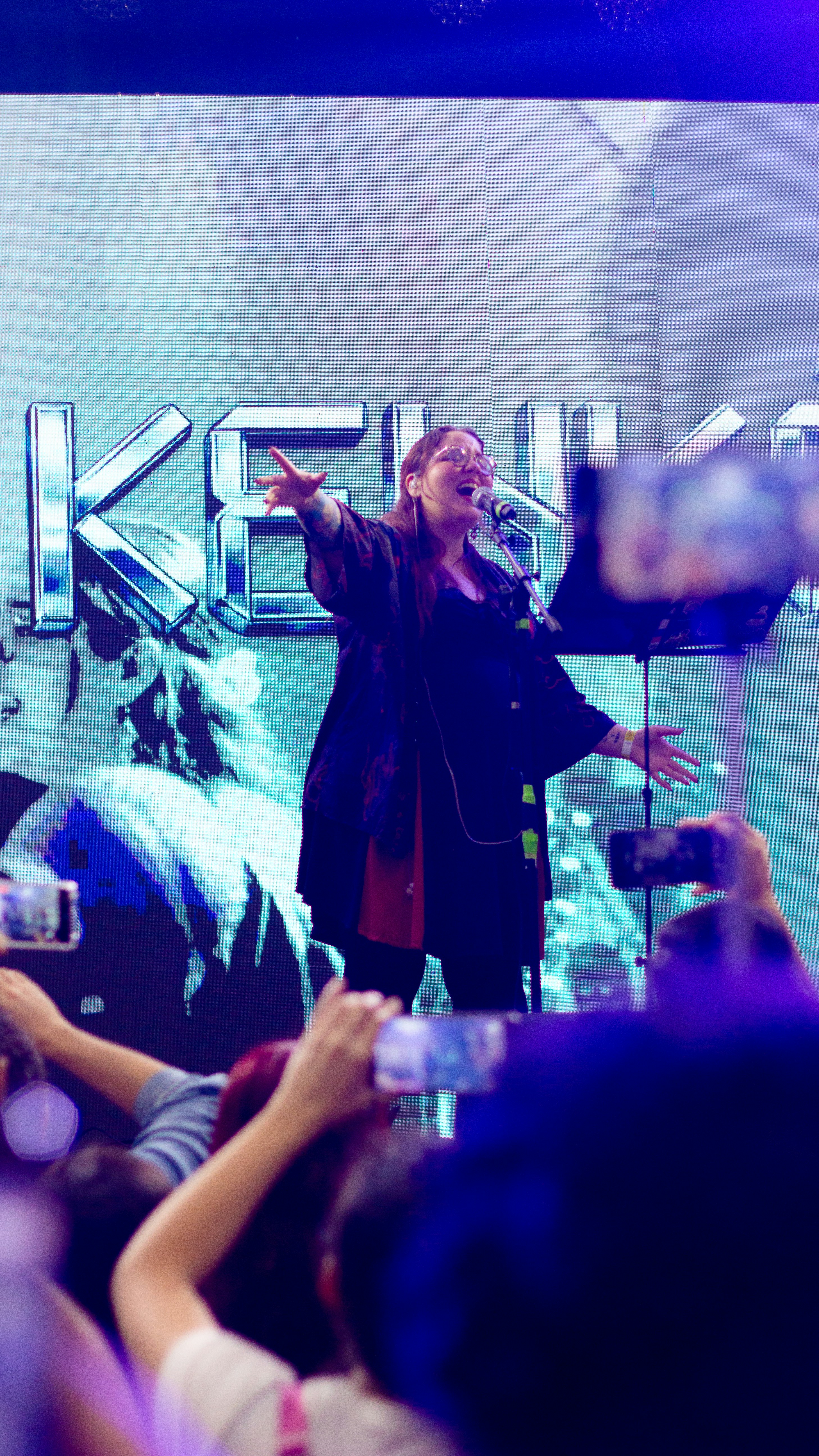 Singer performing on stage with audience holding phones