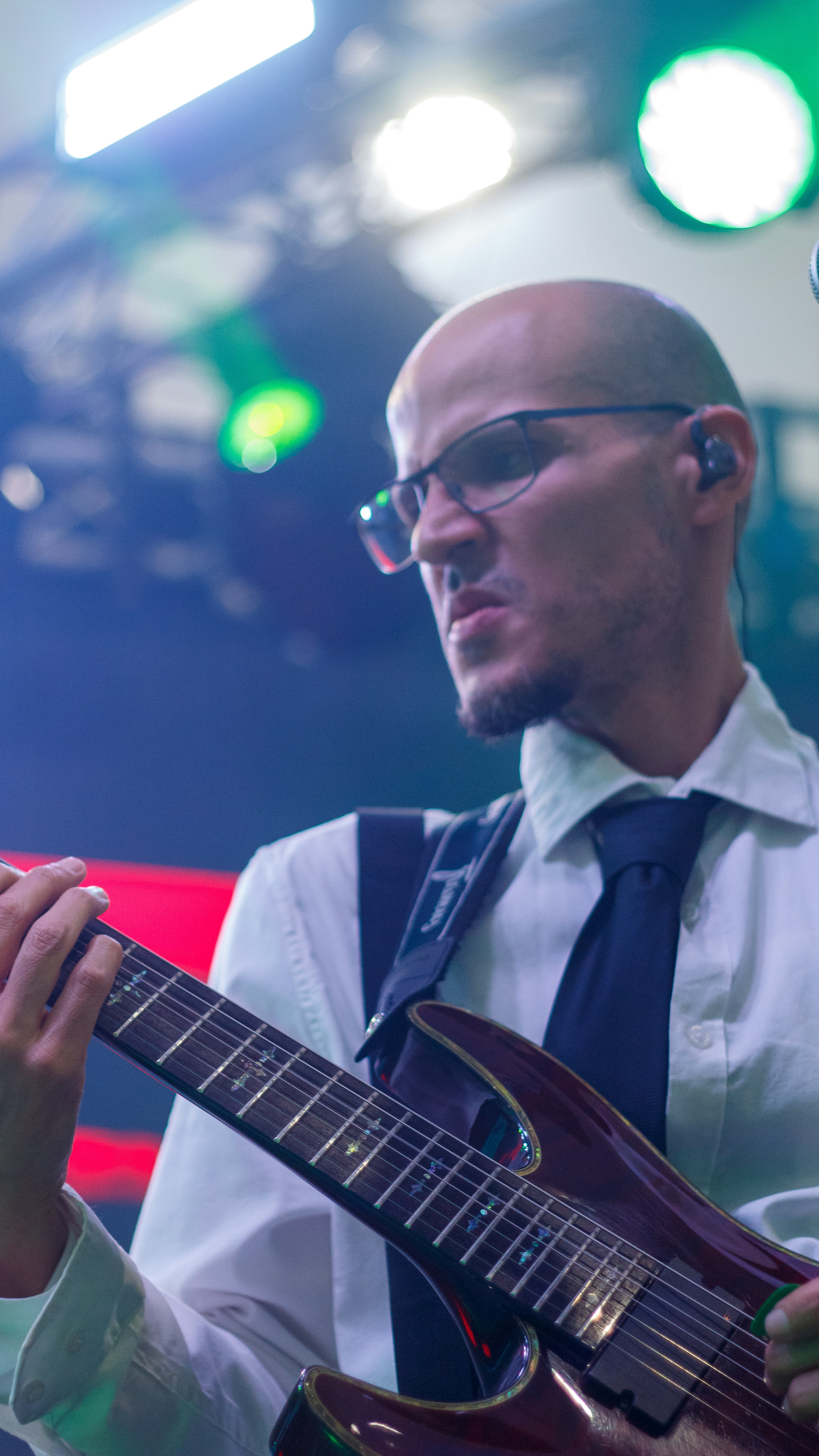 Homem careca de óculos tocando guitarra elétrica no palco.