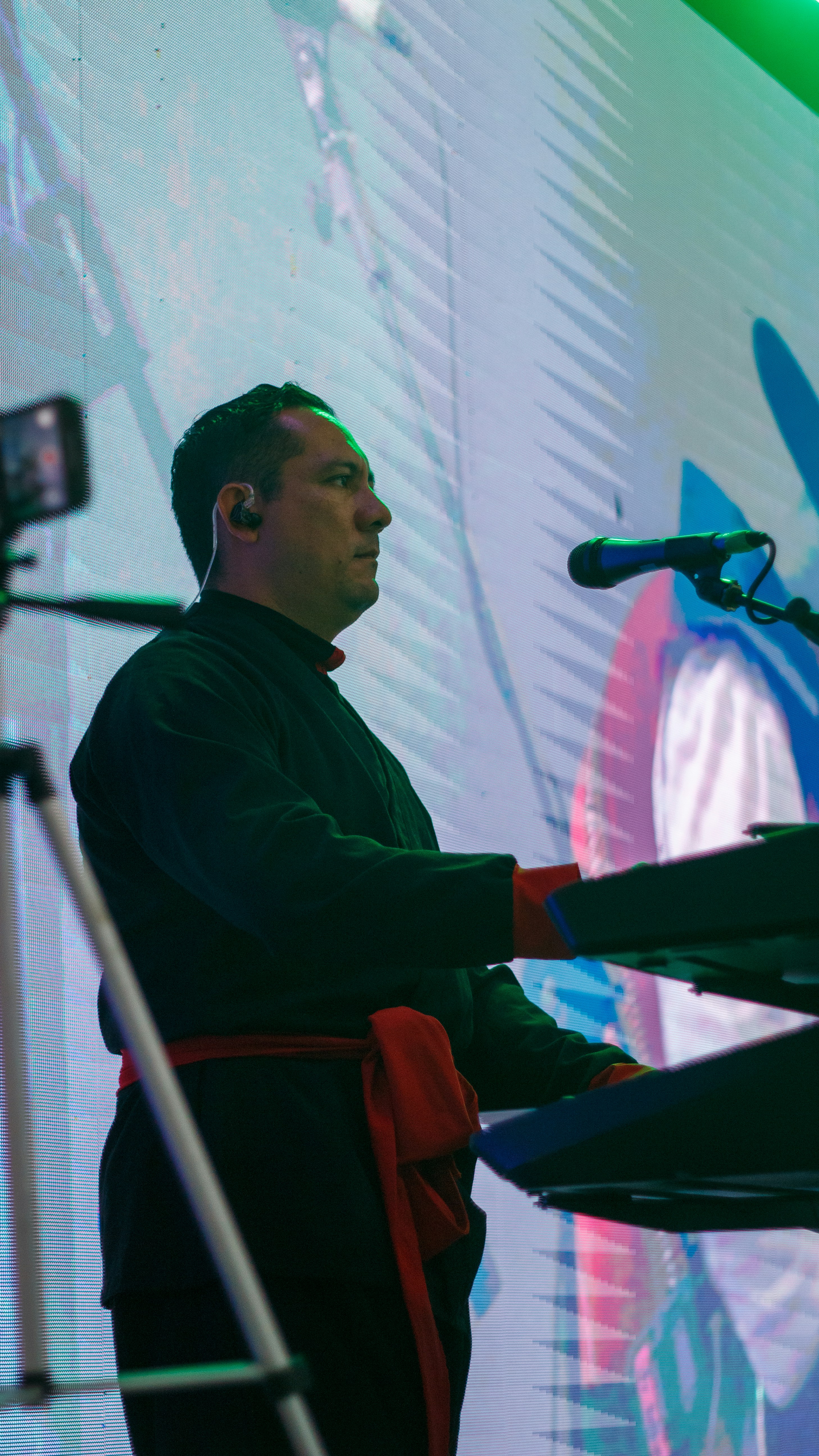 Homem tocando teclado no palco com fundo colorido