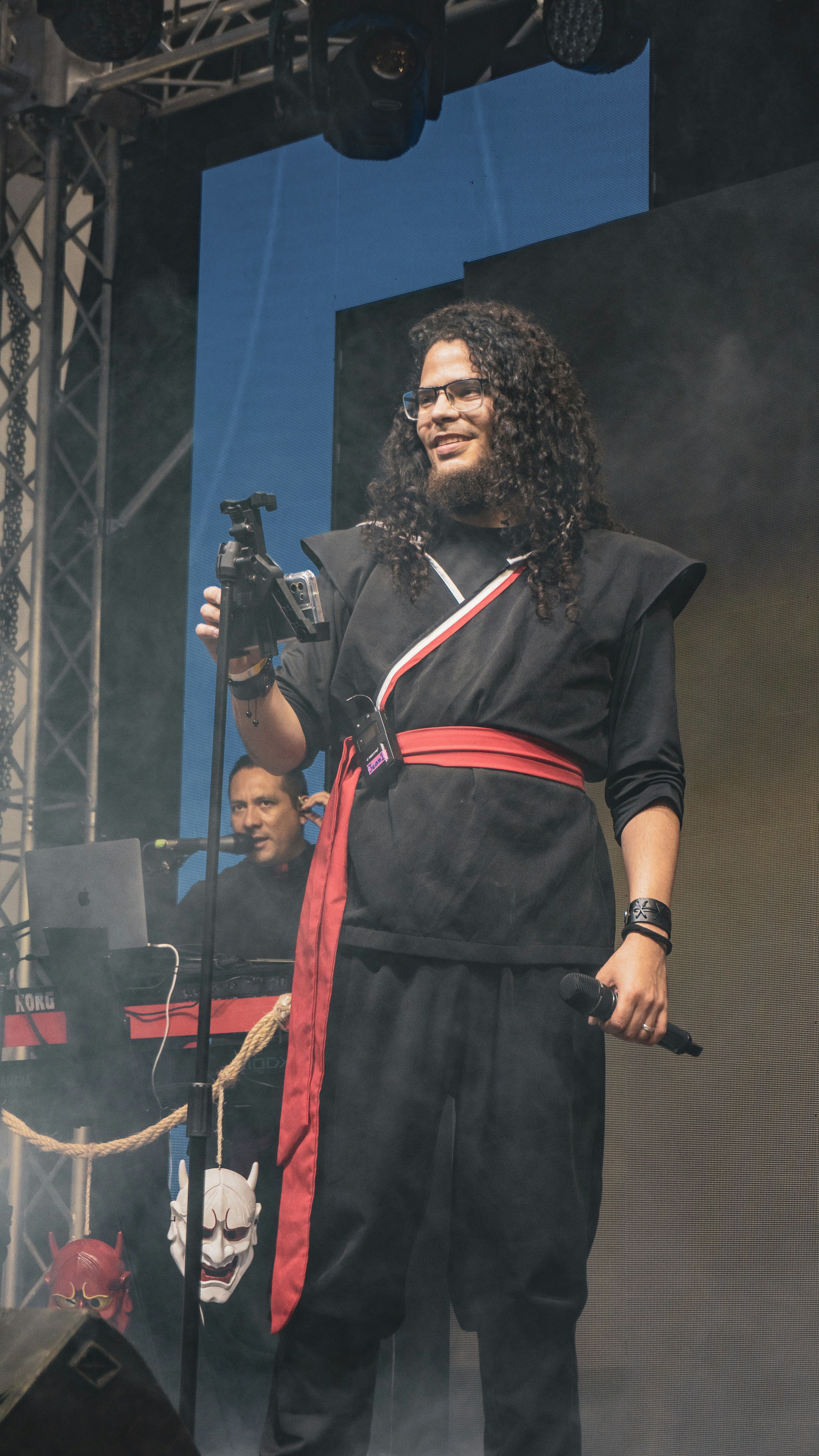Man in black ninja outfit with red sash holding microphone