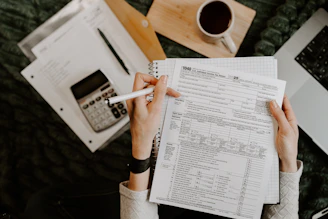 Person reviewing documents with calculator and laptop