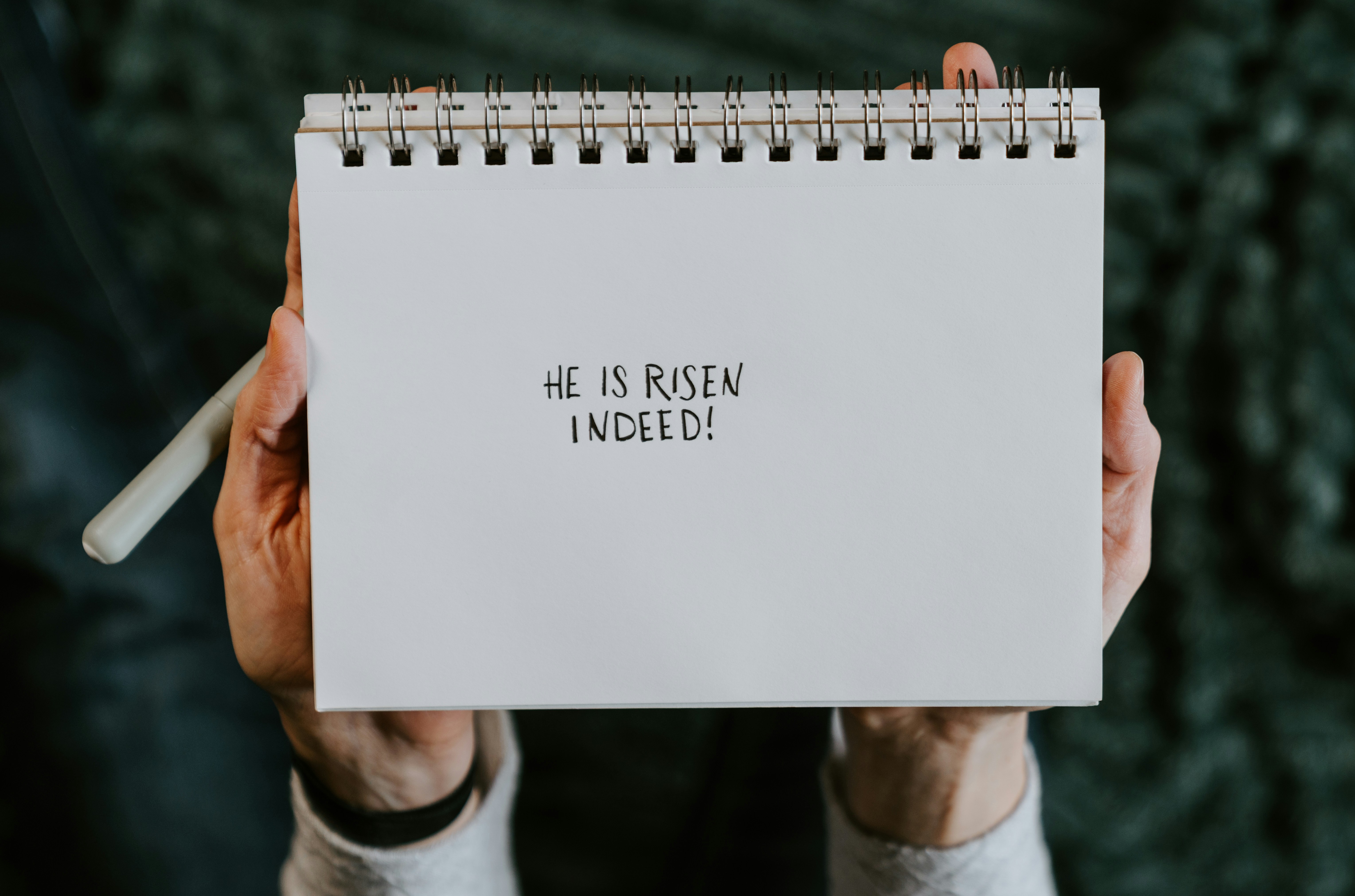 Hands holding a notebook with "he is risen indeed!"