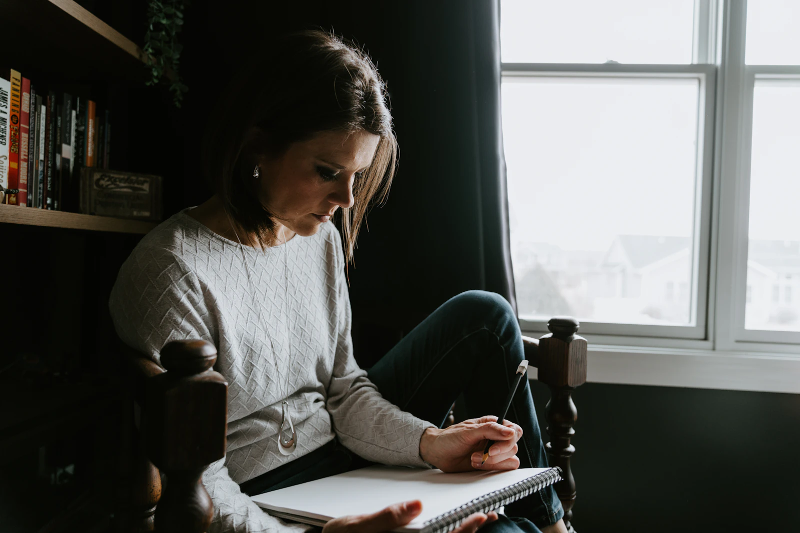 A woman sitting in a chair writing quietly in a notebook