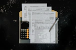 Tax forms with calculator and pen on dark surface