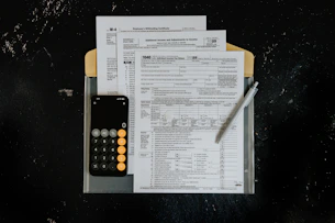 Tax forms with calculator and pen on dark surface