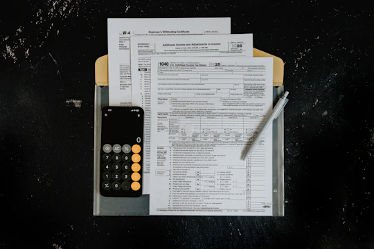 Tax forms with calculator and pen on dark surface