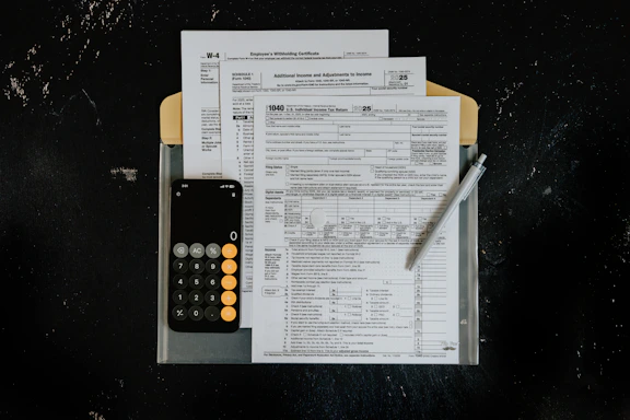 Tax forms with calculator and pen on dark surface