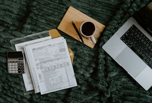 Laptop, papers, calculator, and coffee on blanket.