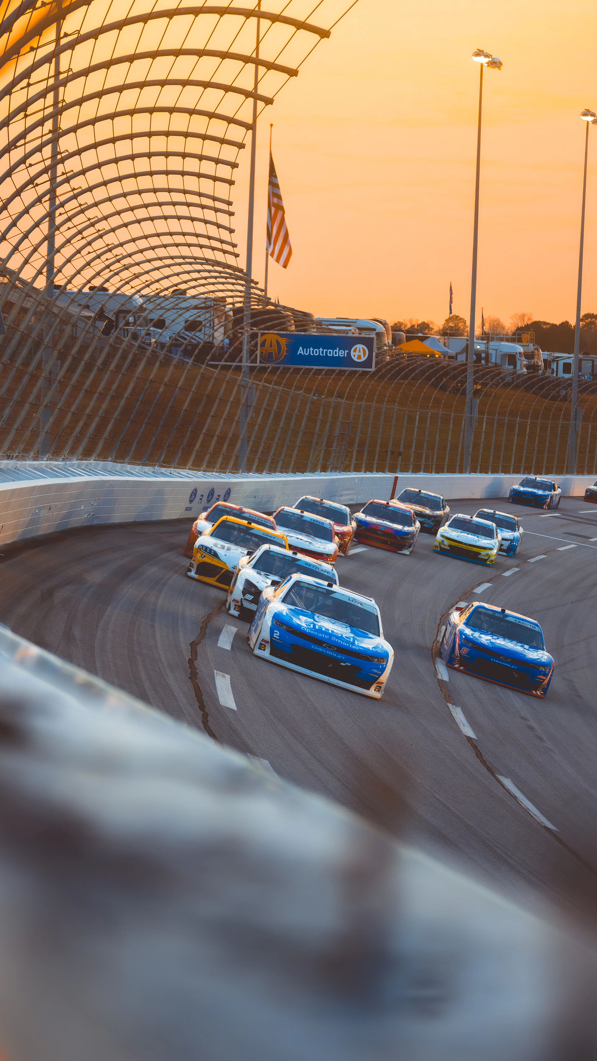 Race cars speed around a track at sunset