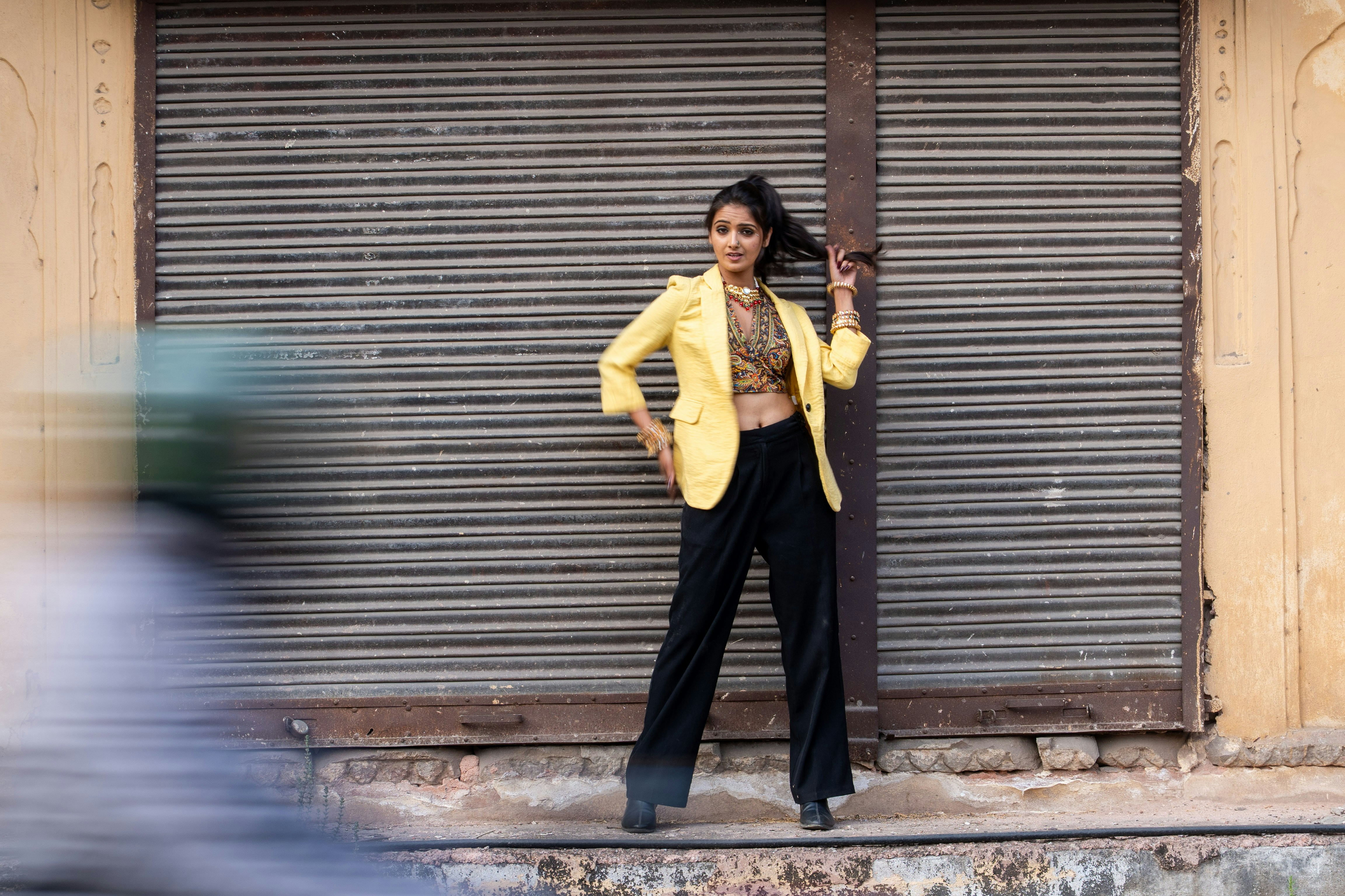 Woman in yellow blazer stands against metal shutter.