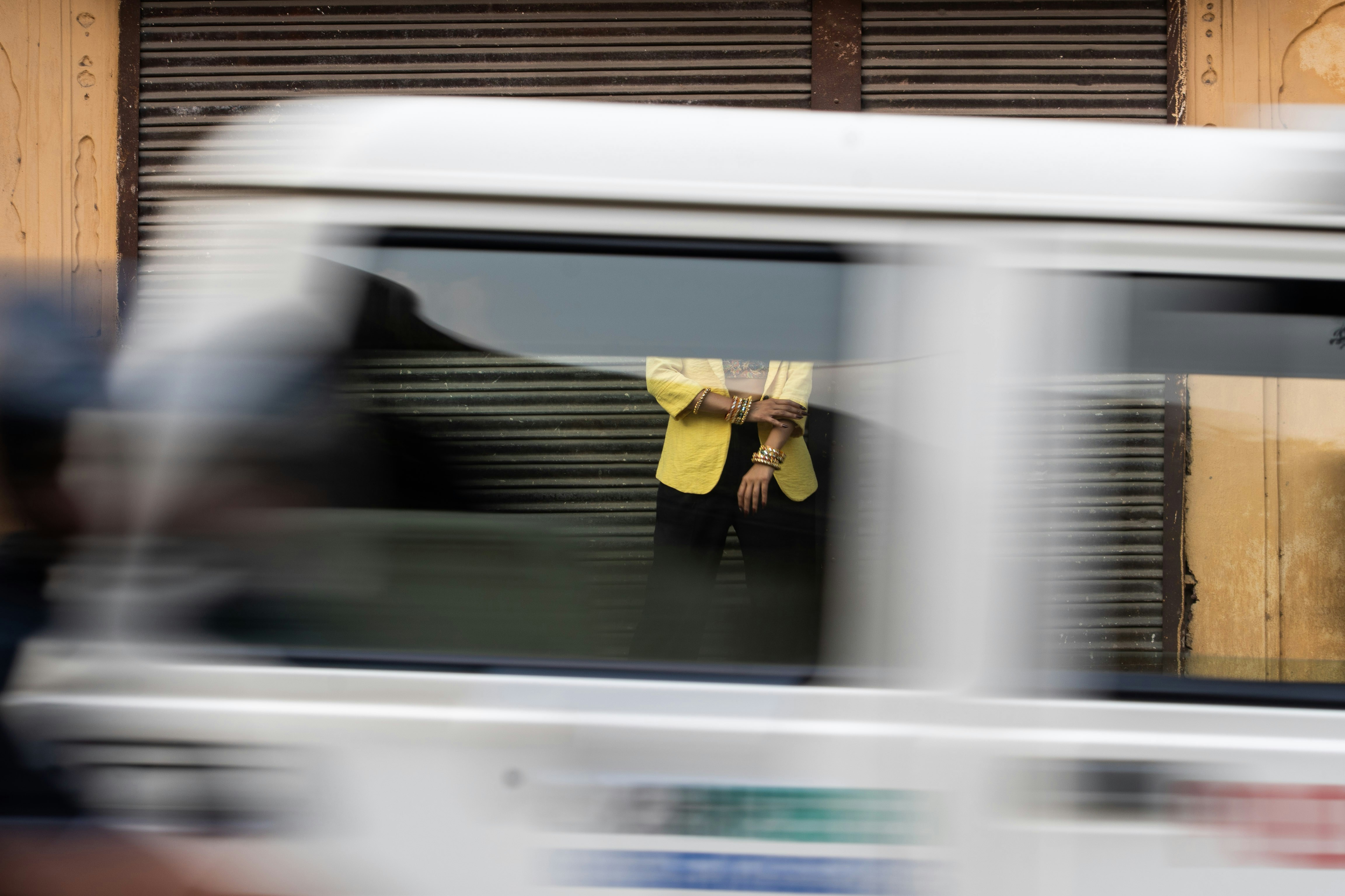Person in yellow shirt seen through moving vehicle window.