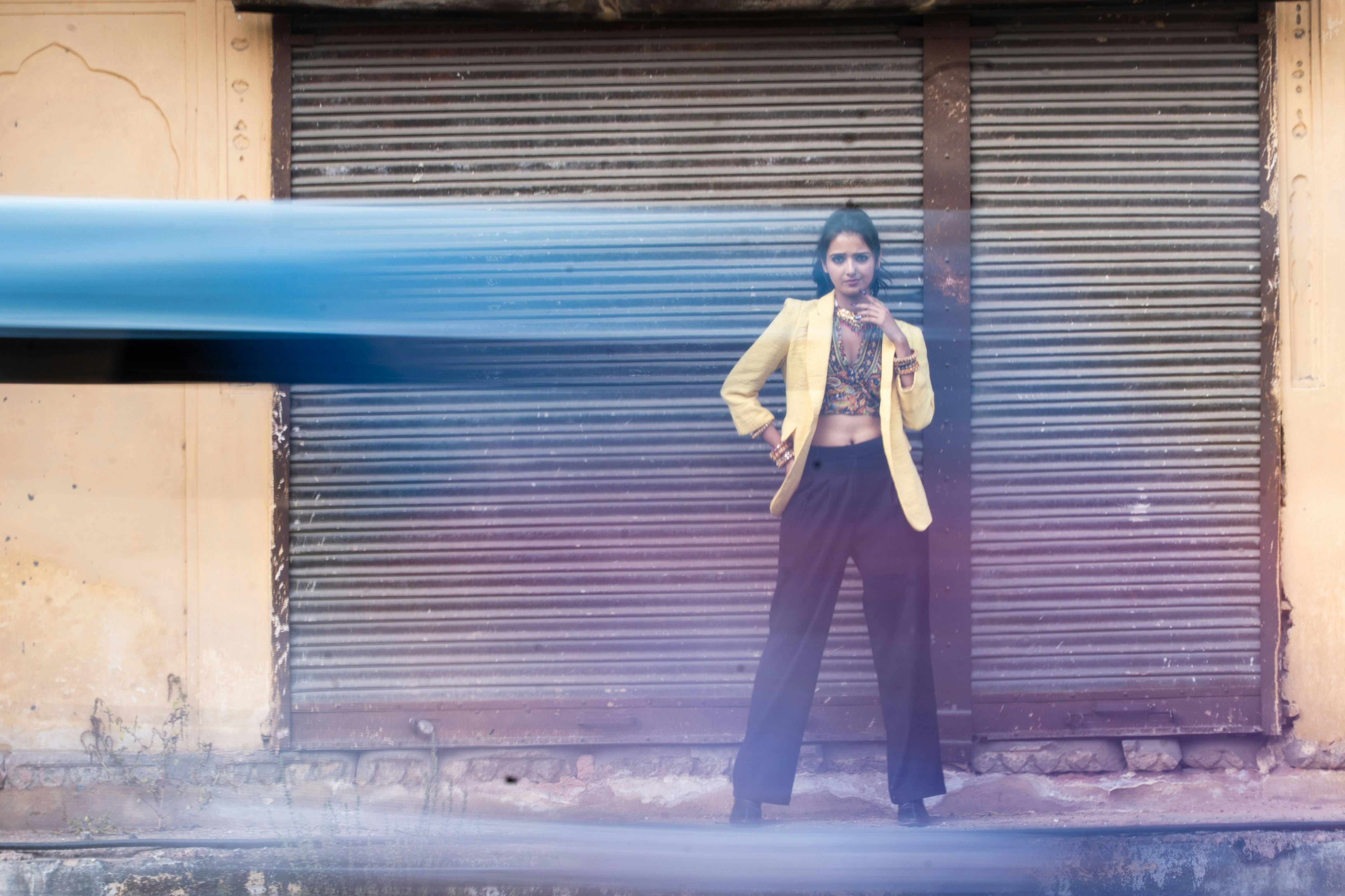 Woman in yellow jacket stands against shuttered wall