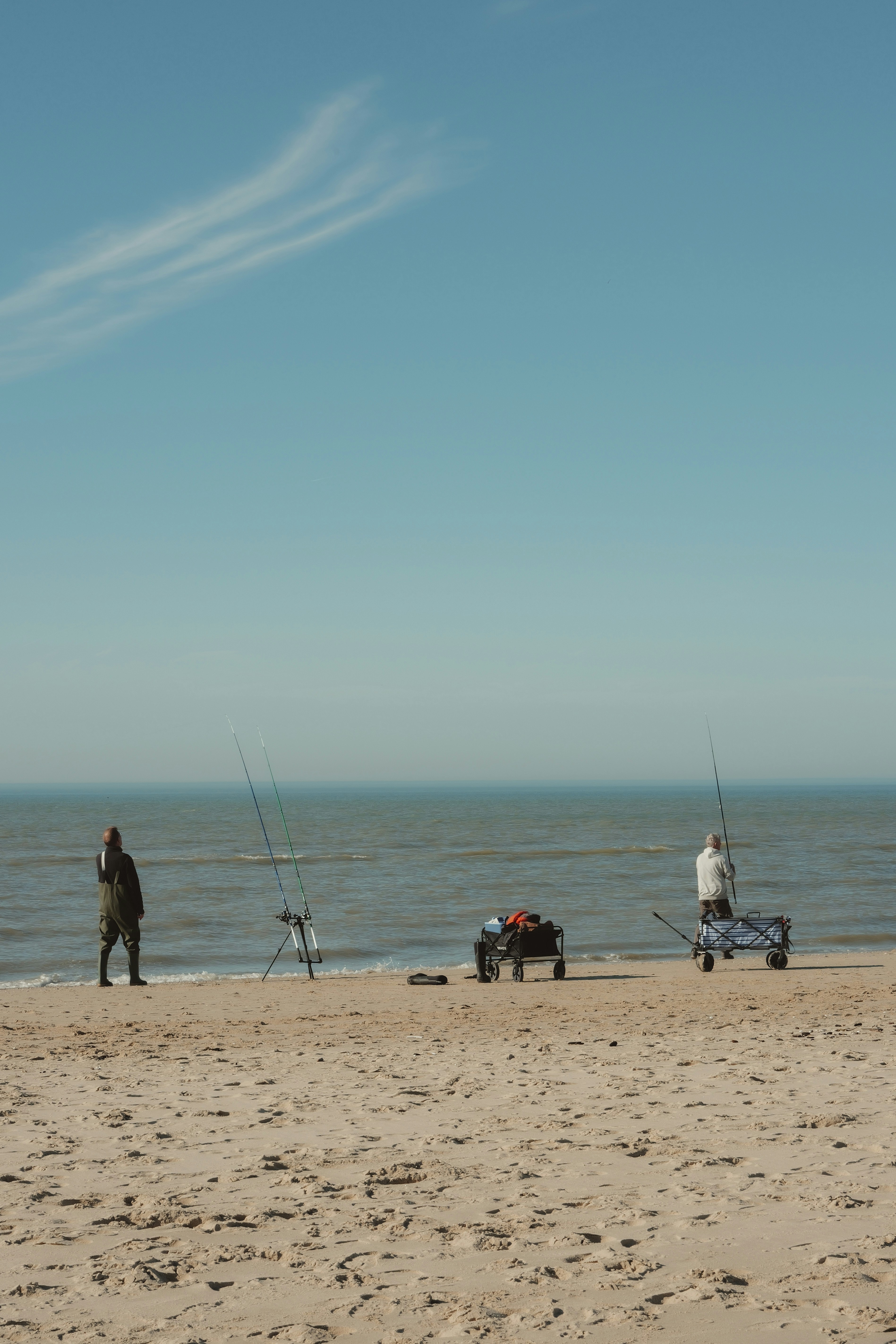 Two people fishing on a sandy beach by the ocean.