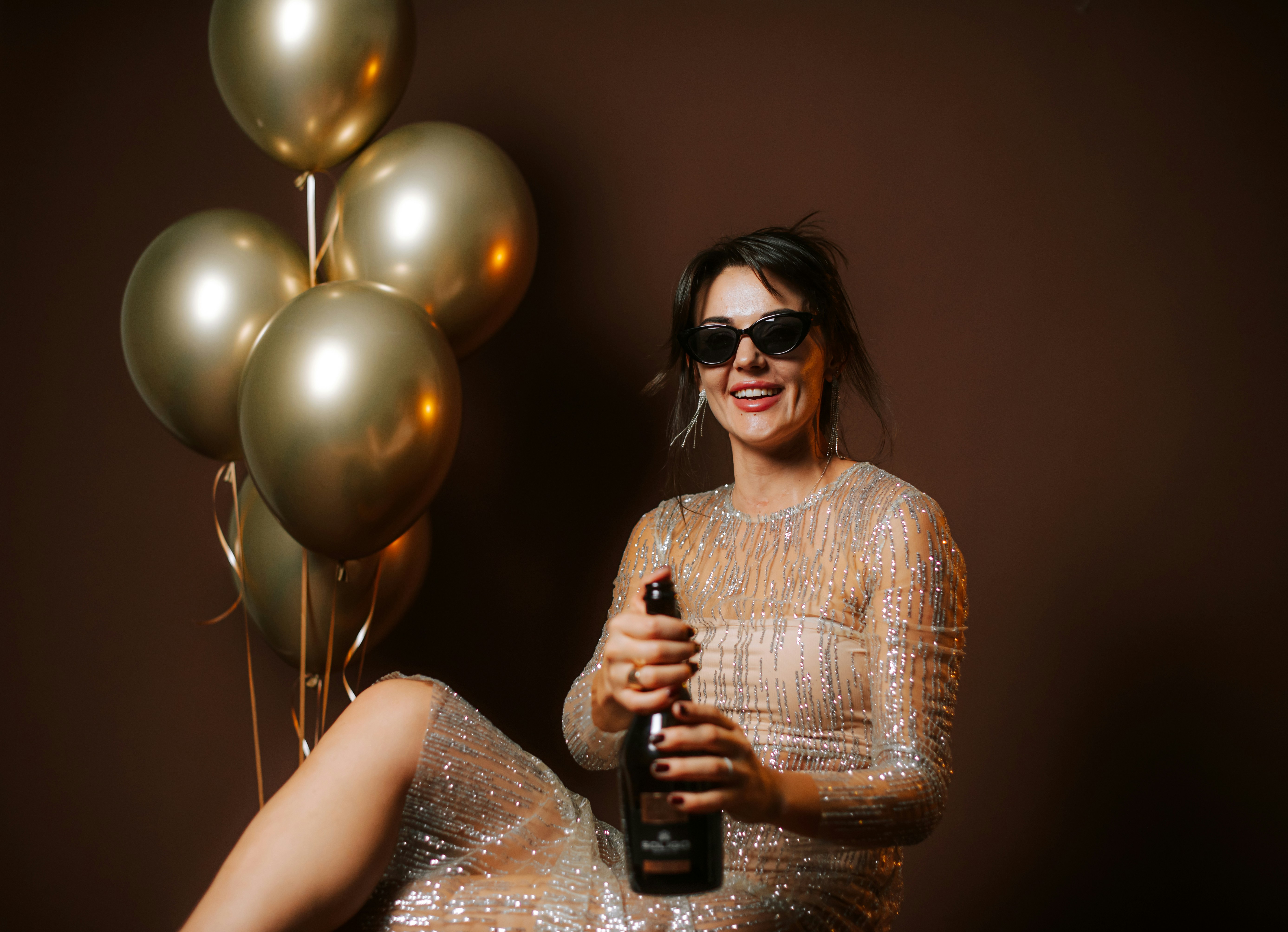 Mulher com vestido brilhante abrindo garrafa de champanhe com balões