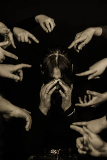 Person surrounded by pointing fingers in dark setting