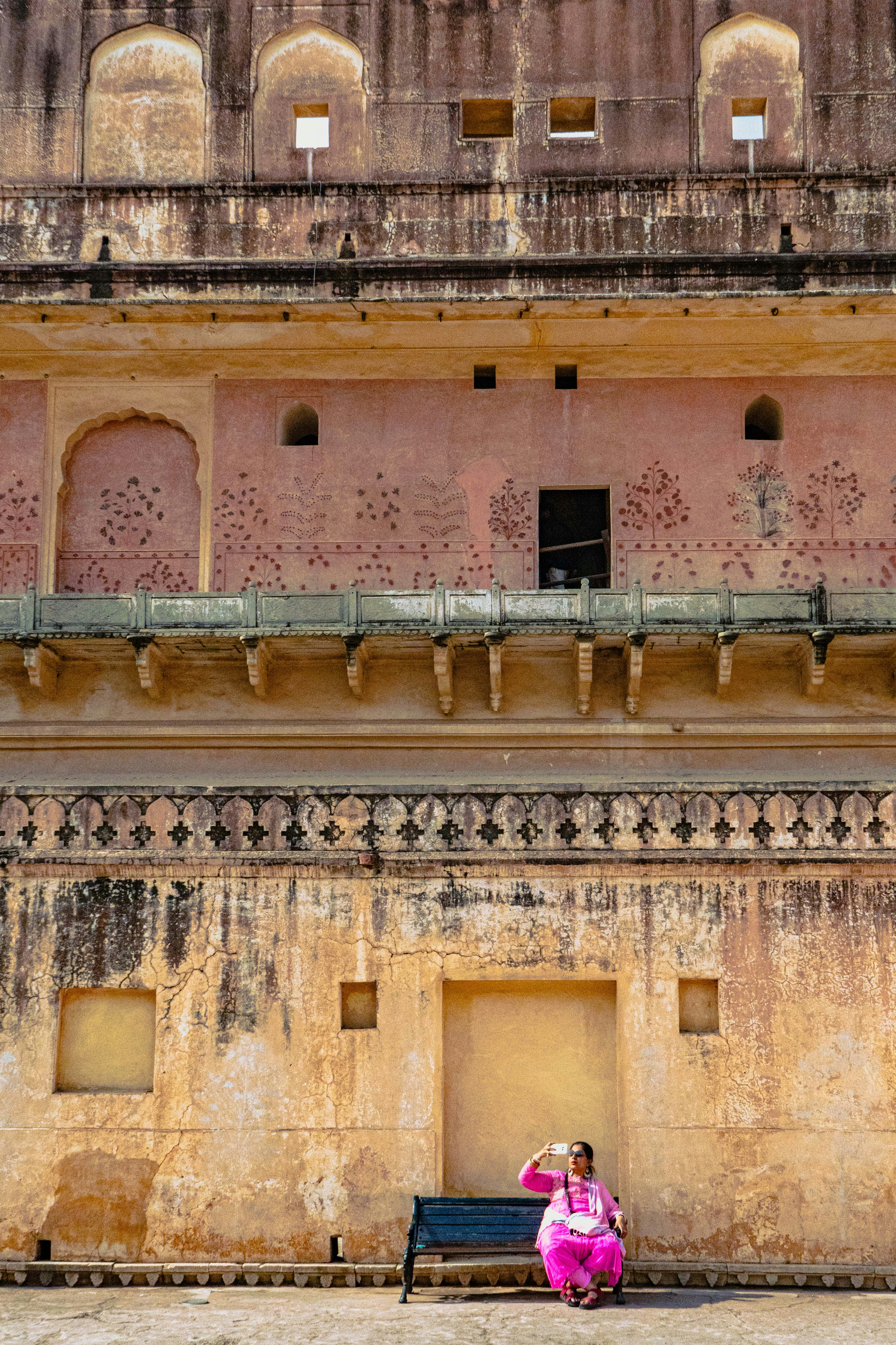 Frau in Rosa sitzt auf einer Bank in der Nähe des alten Gebäudes