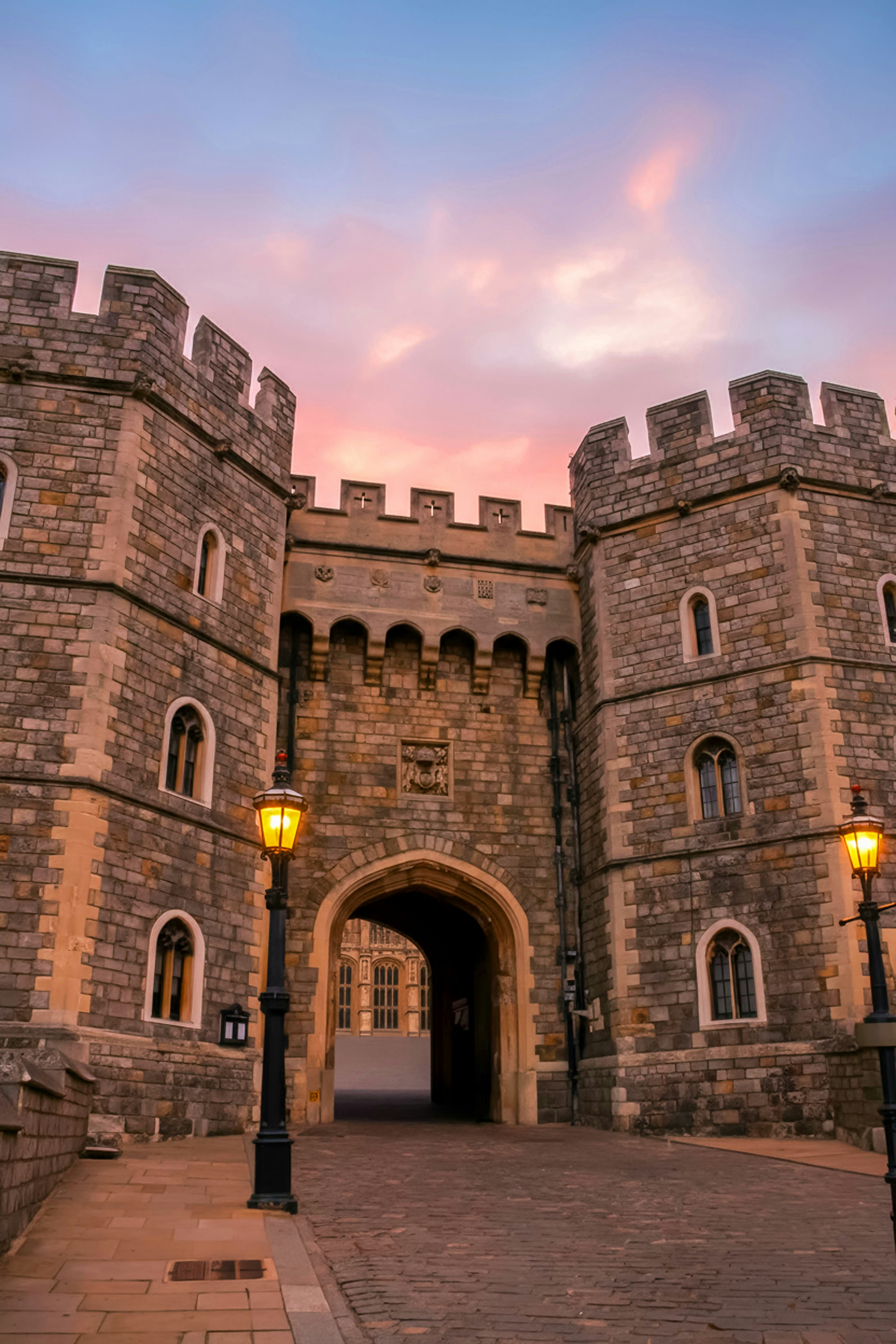 Stone castle gate with ornate lamps at sunset