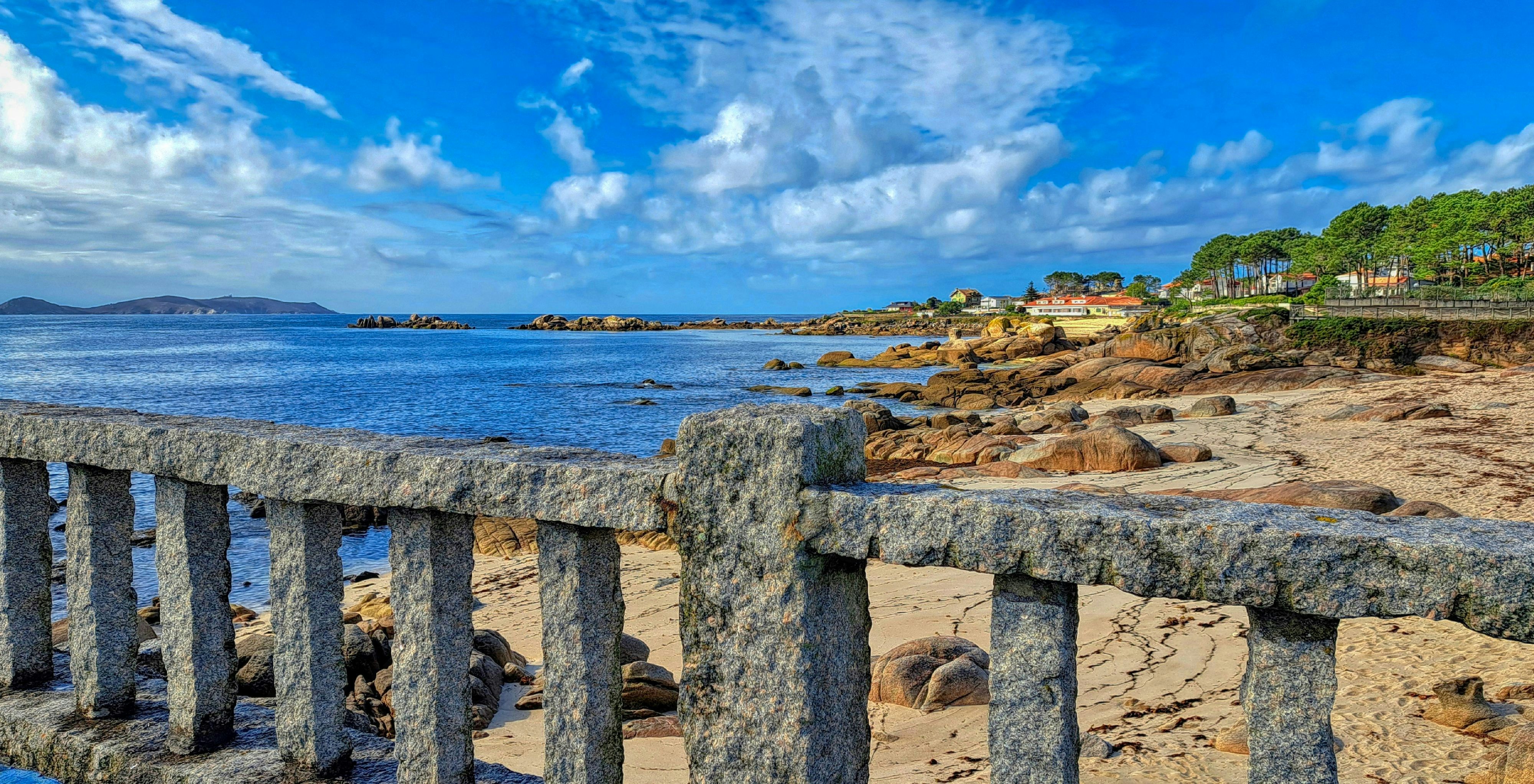 Stone railing overlooks a rocky beach and blue ocean.