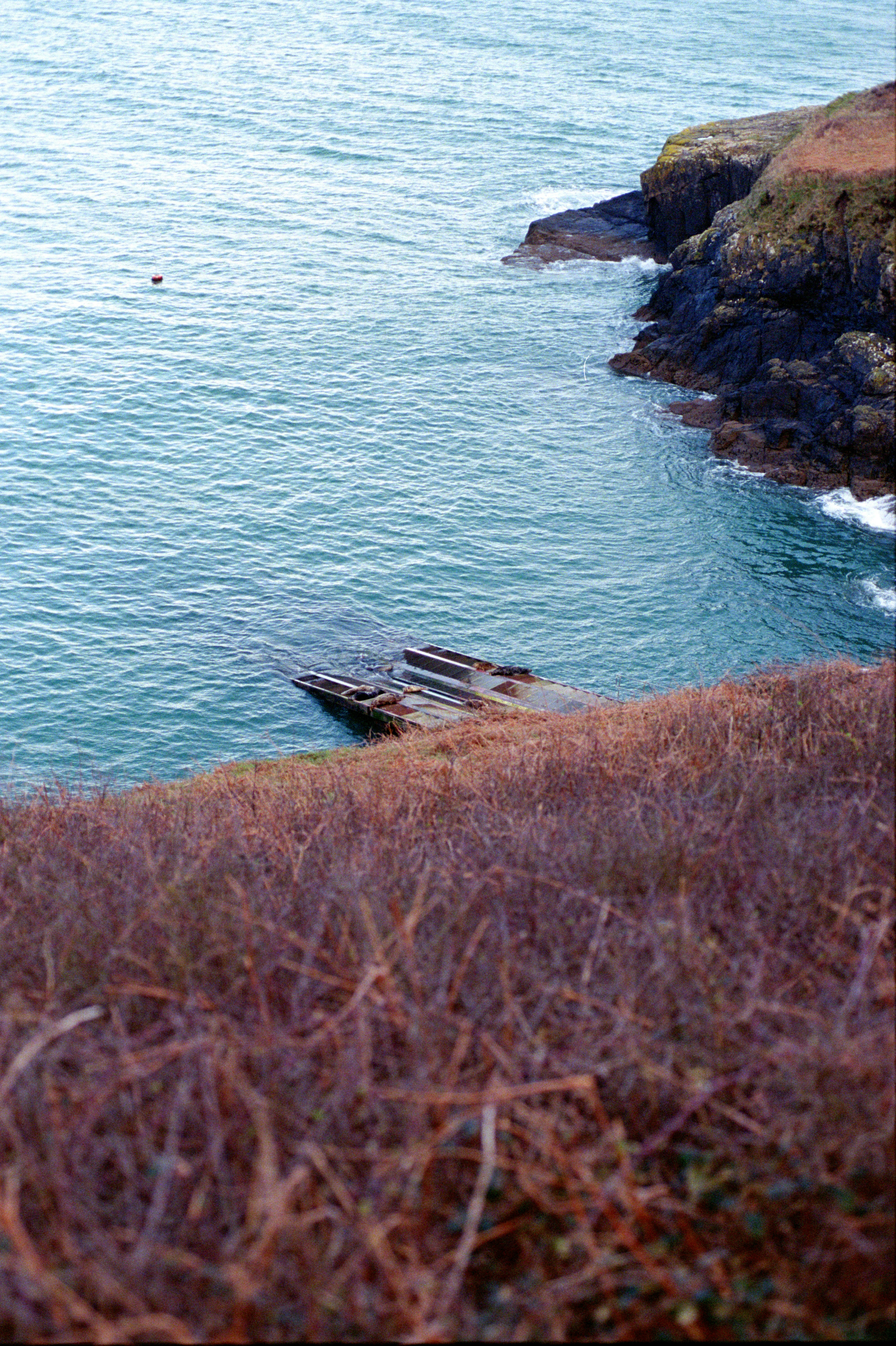 Sunken ship hull near rocky coastline with dry grass