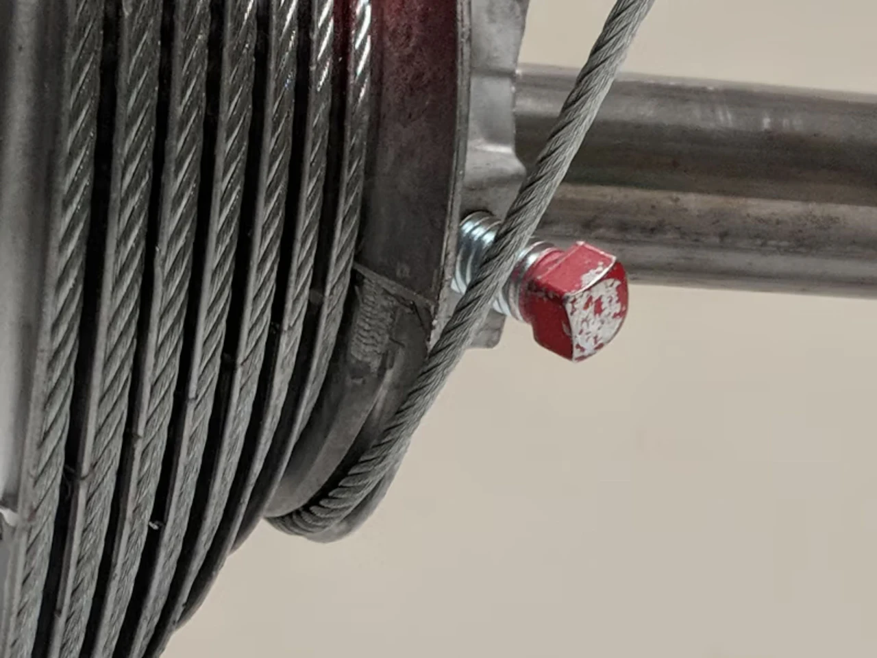 A steel lift cable wound on its drum on a residential garage door, with the set screw visible