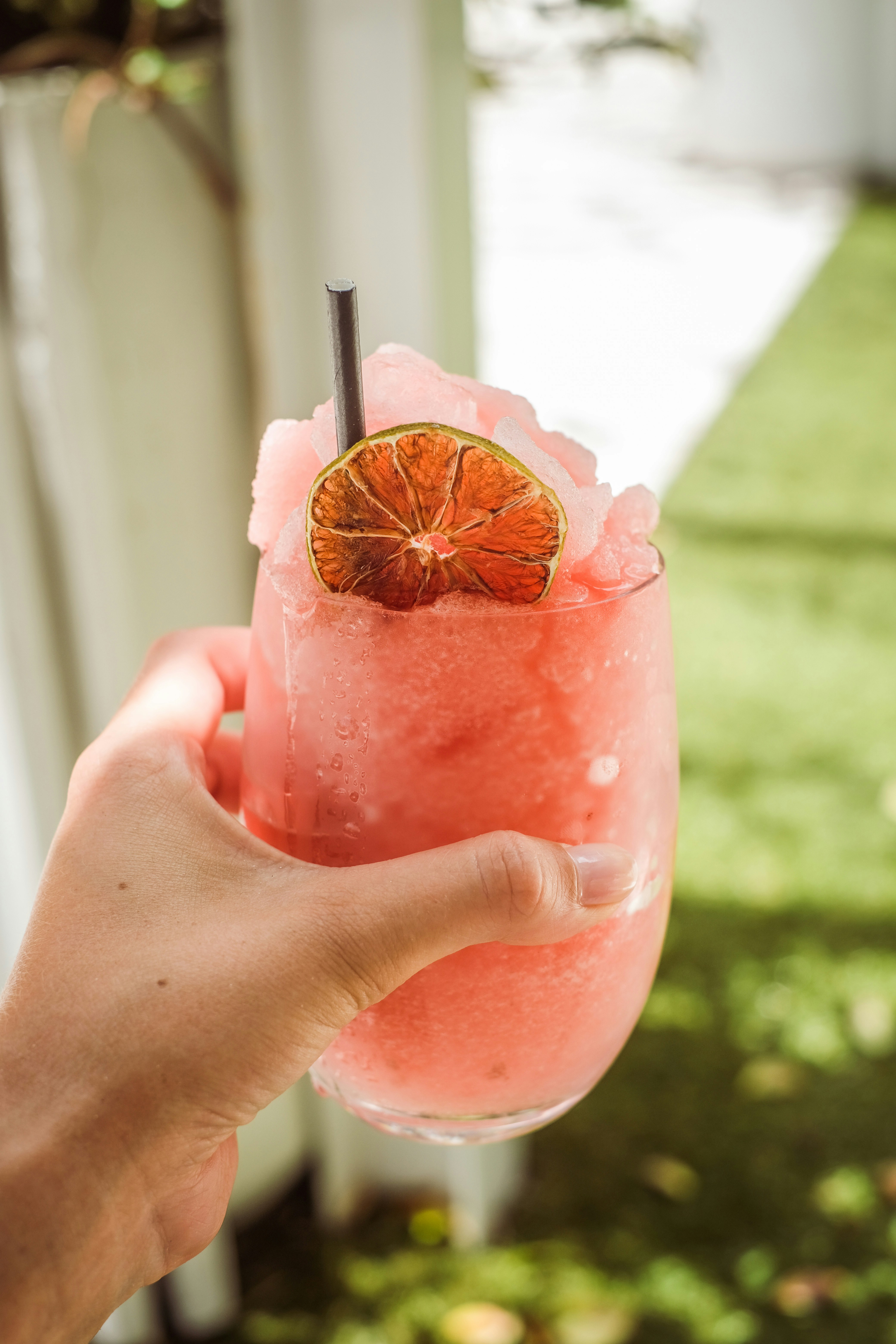 Hand holding a pink frozen cocktail with lime garnish