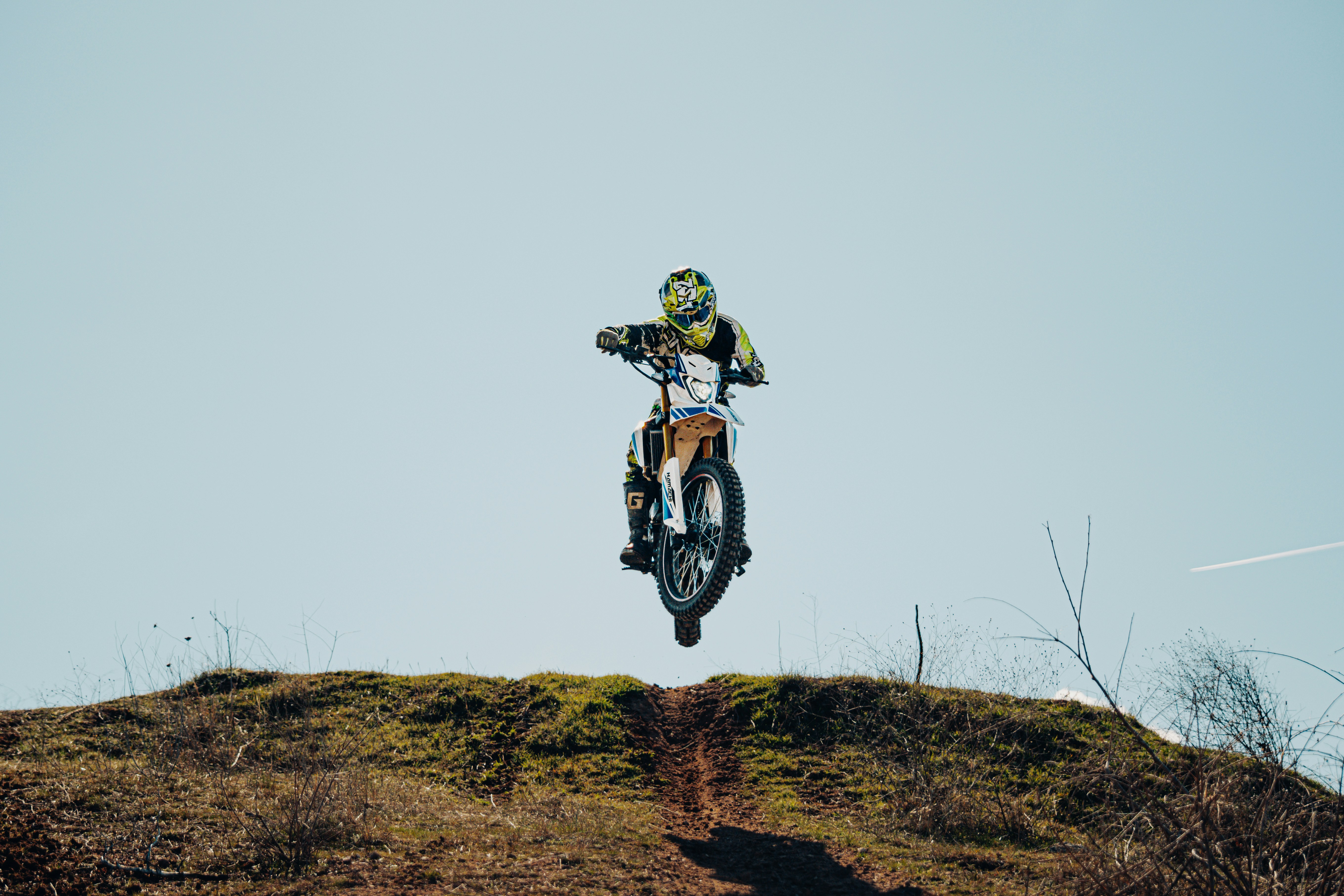 Motocross rider jumps over a dirt hill against sky
