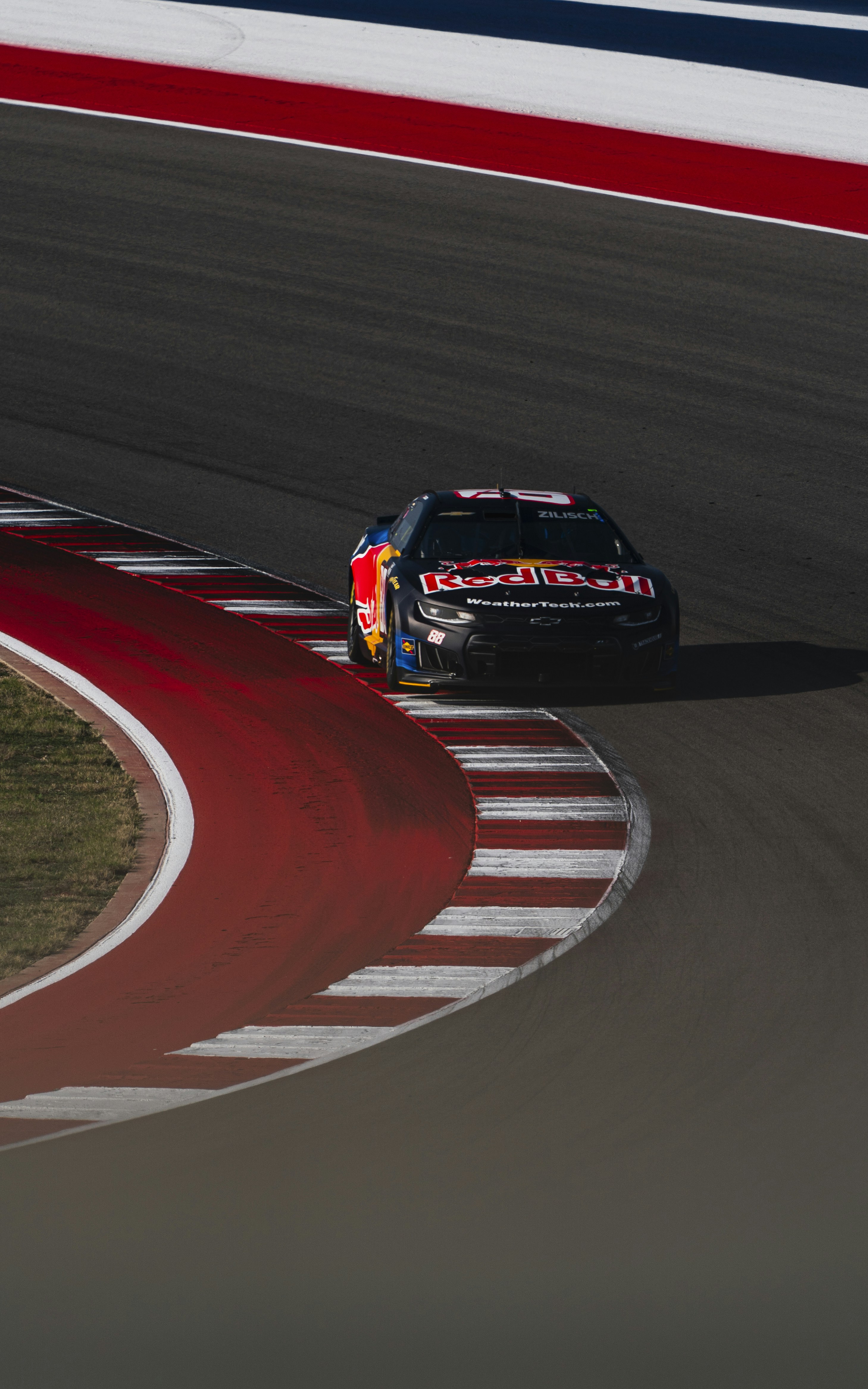 Race car with red bull branding speeds around a track.