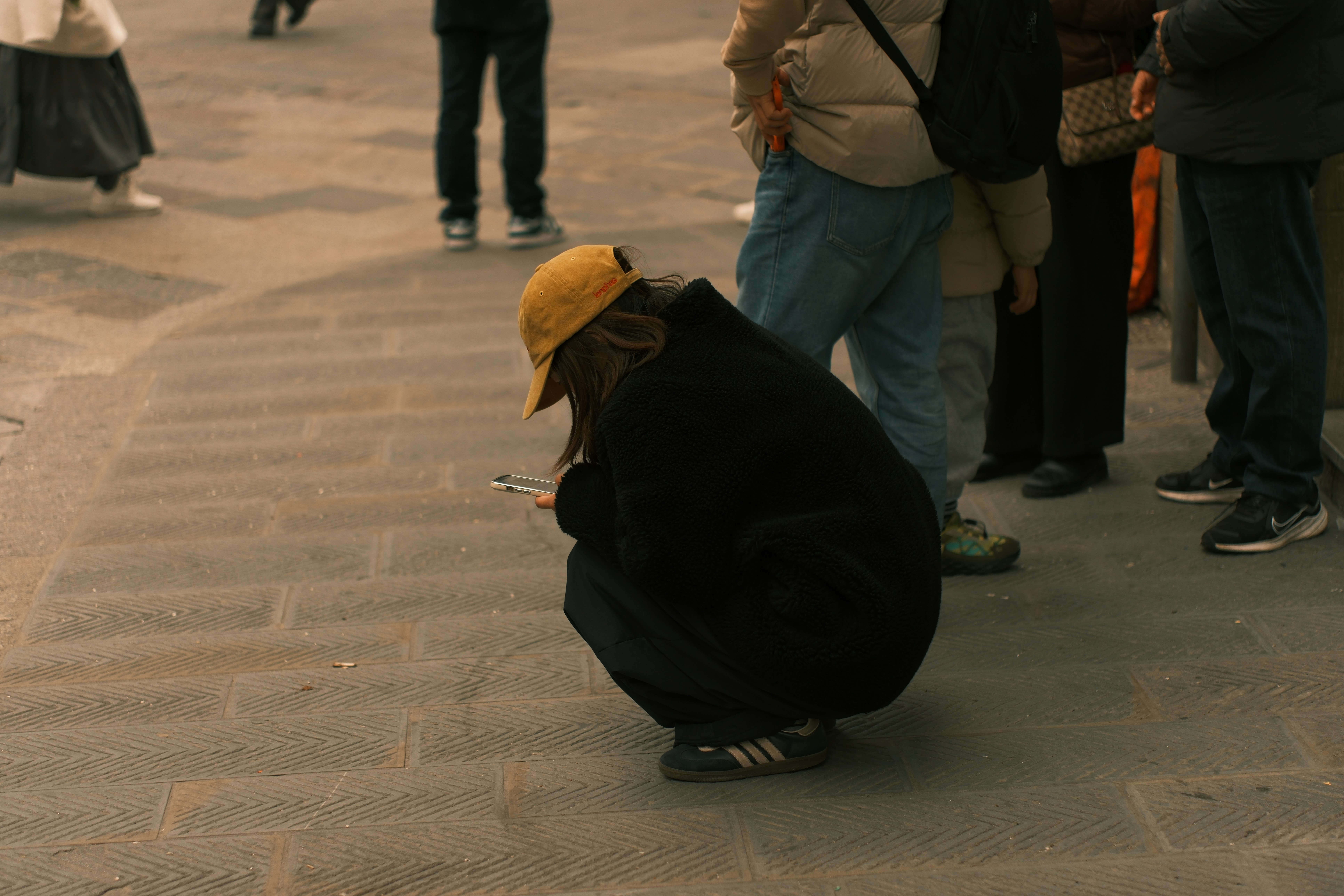 Person in yellow hat crouches, looking at phone.