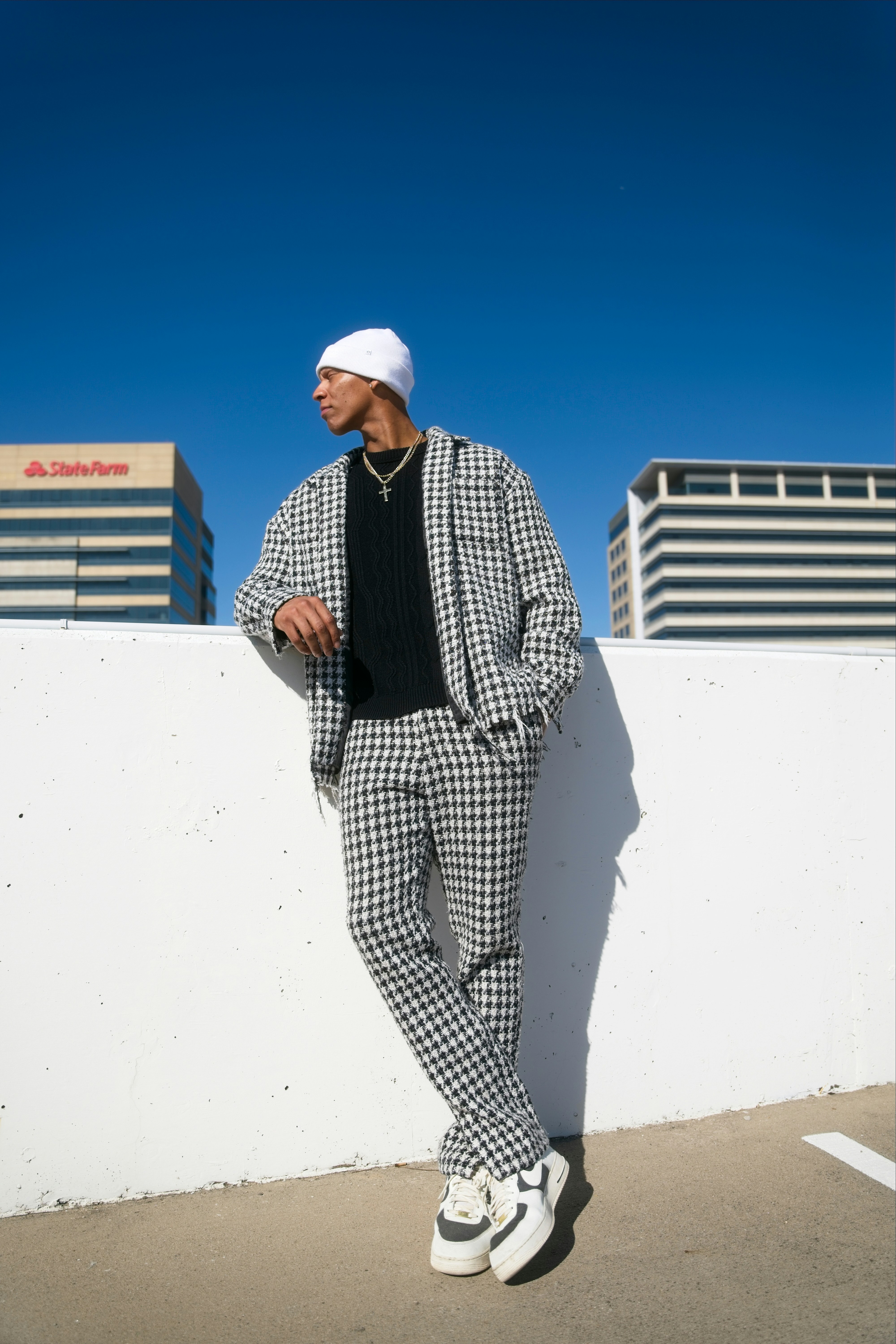 Man in checkered suit leans against wall outdoors.