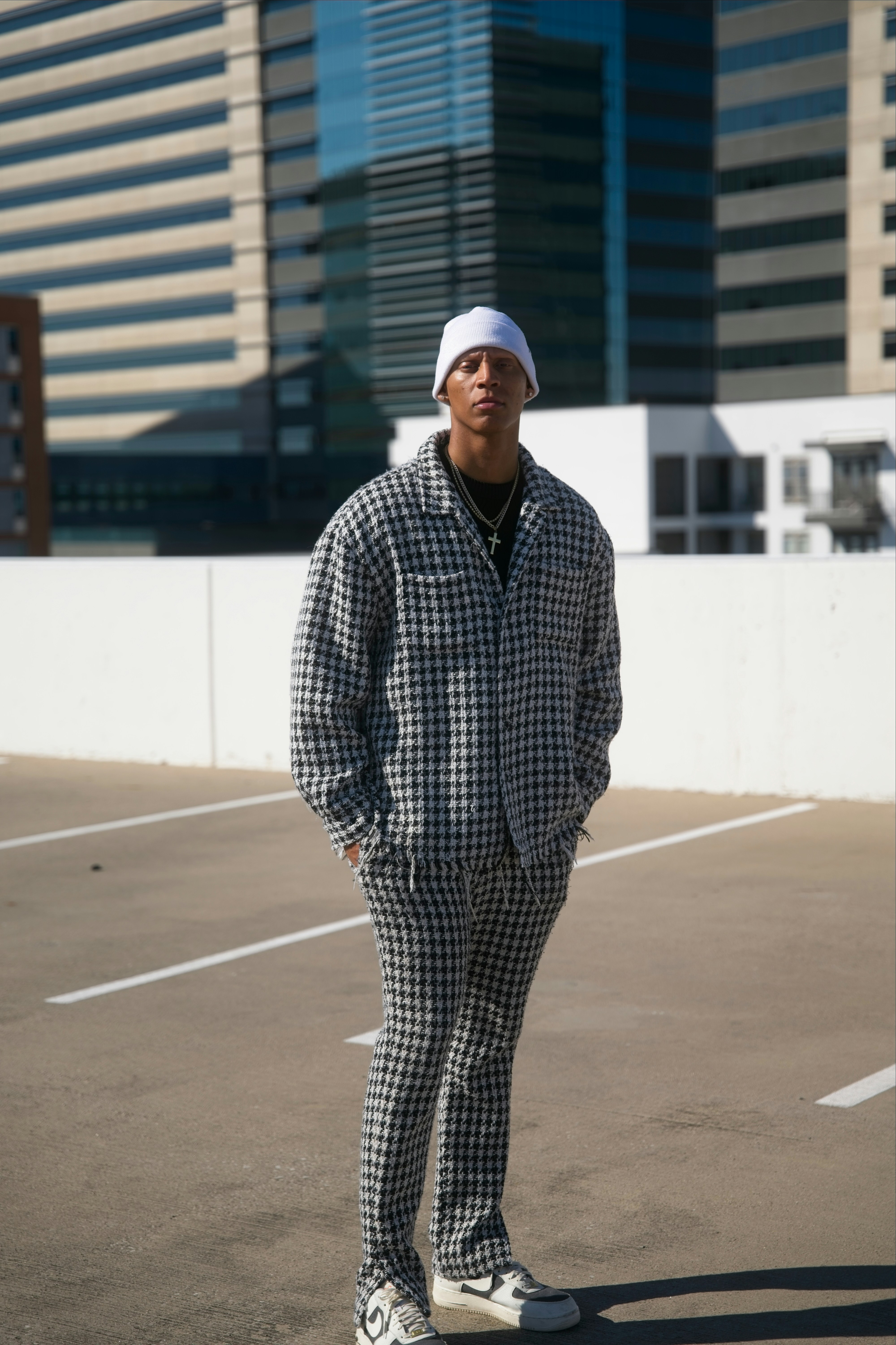 Homem de terno xadrez parado em estacionamento urbano