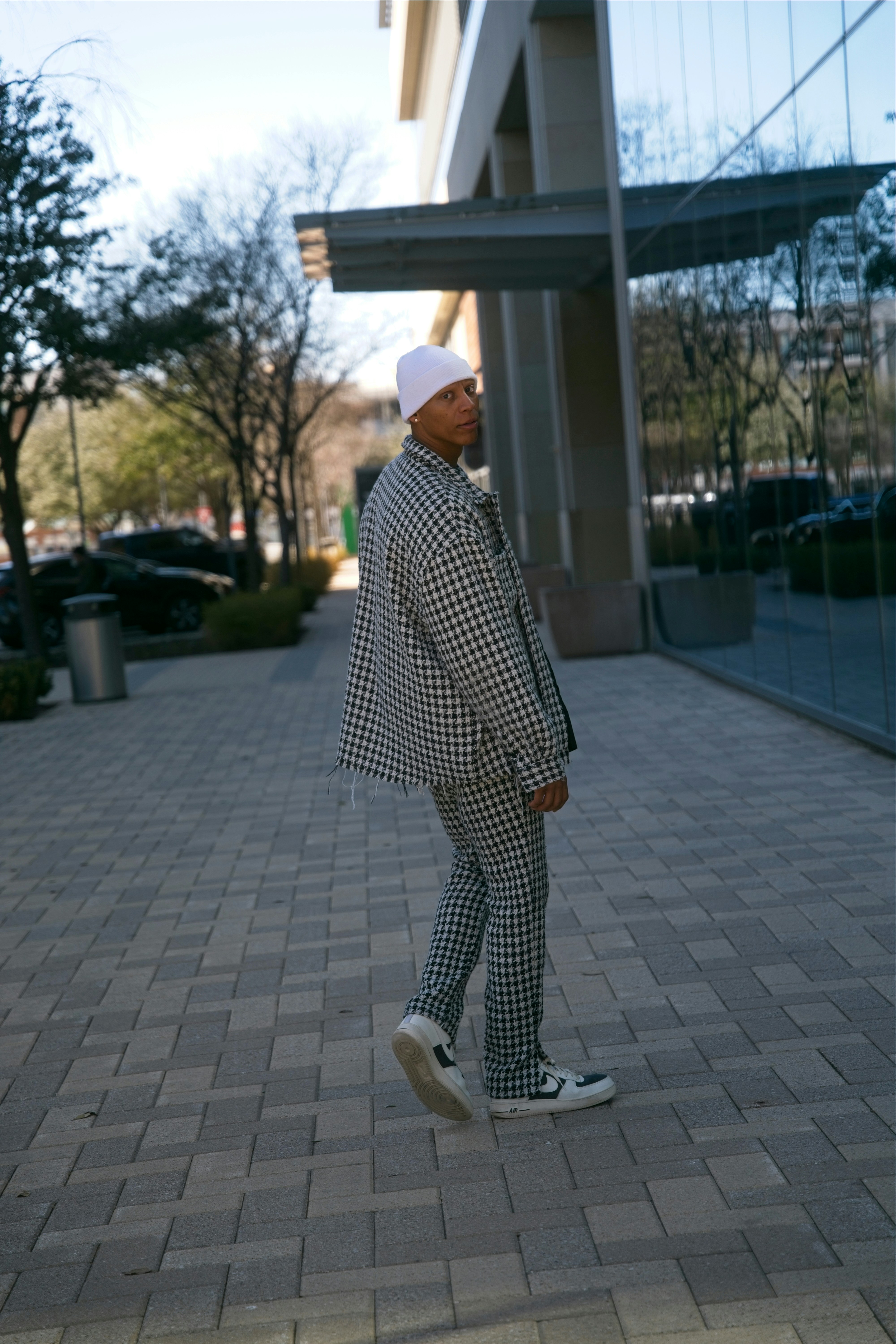 Homem com roupa xadrez anda na calçada perto do prédio