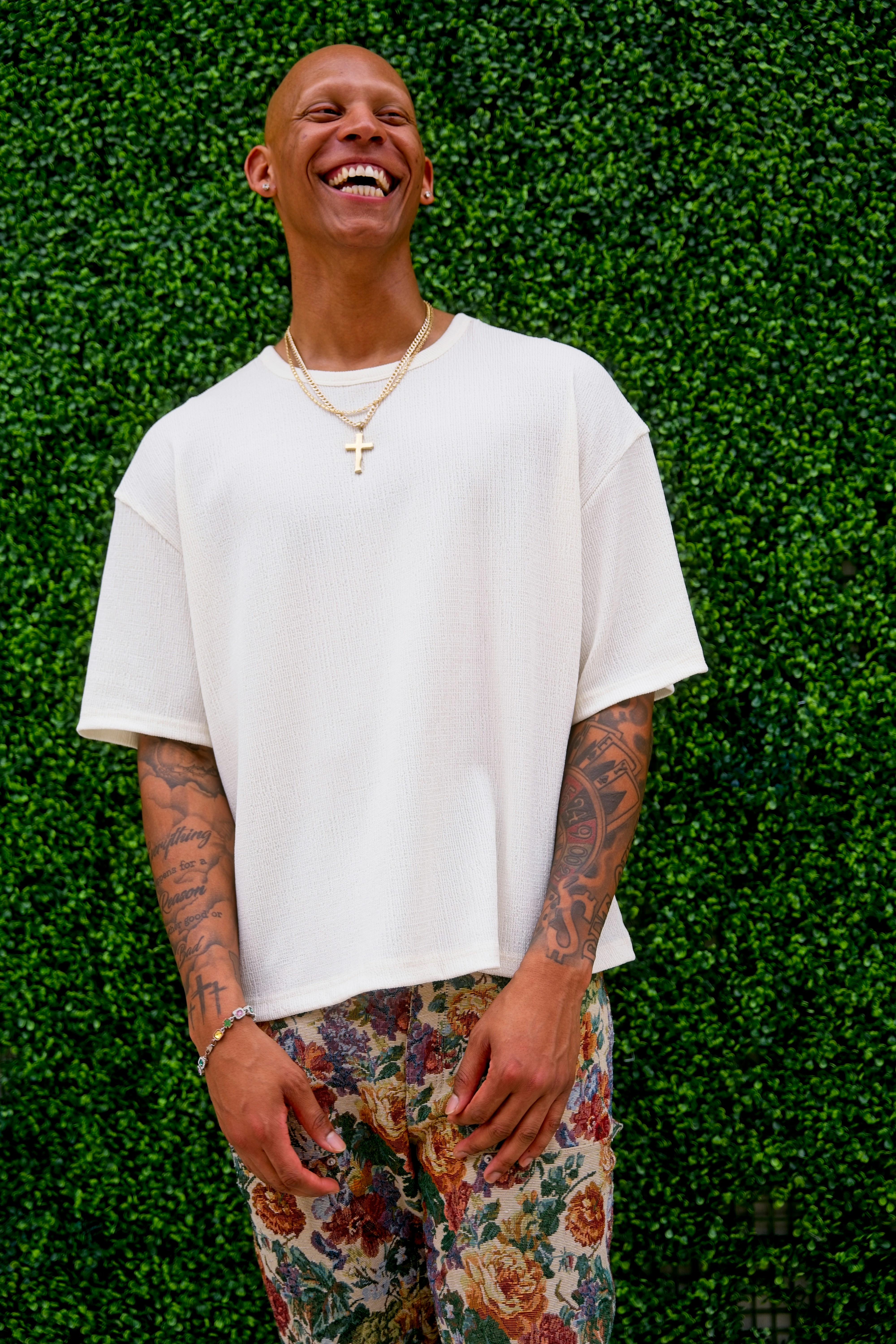 Um homem sorridente com tatuagens em uma camisa creme.
