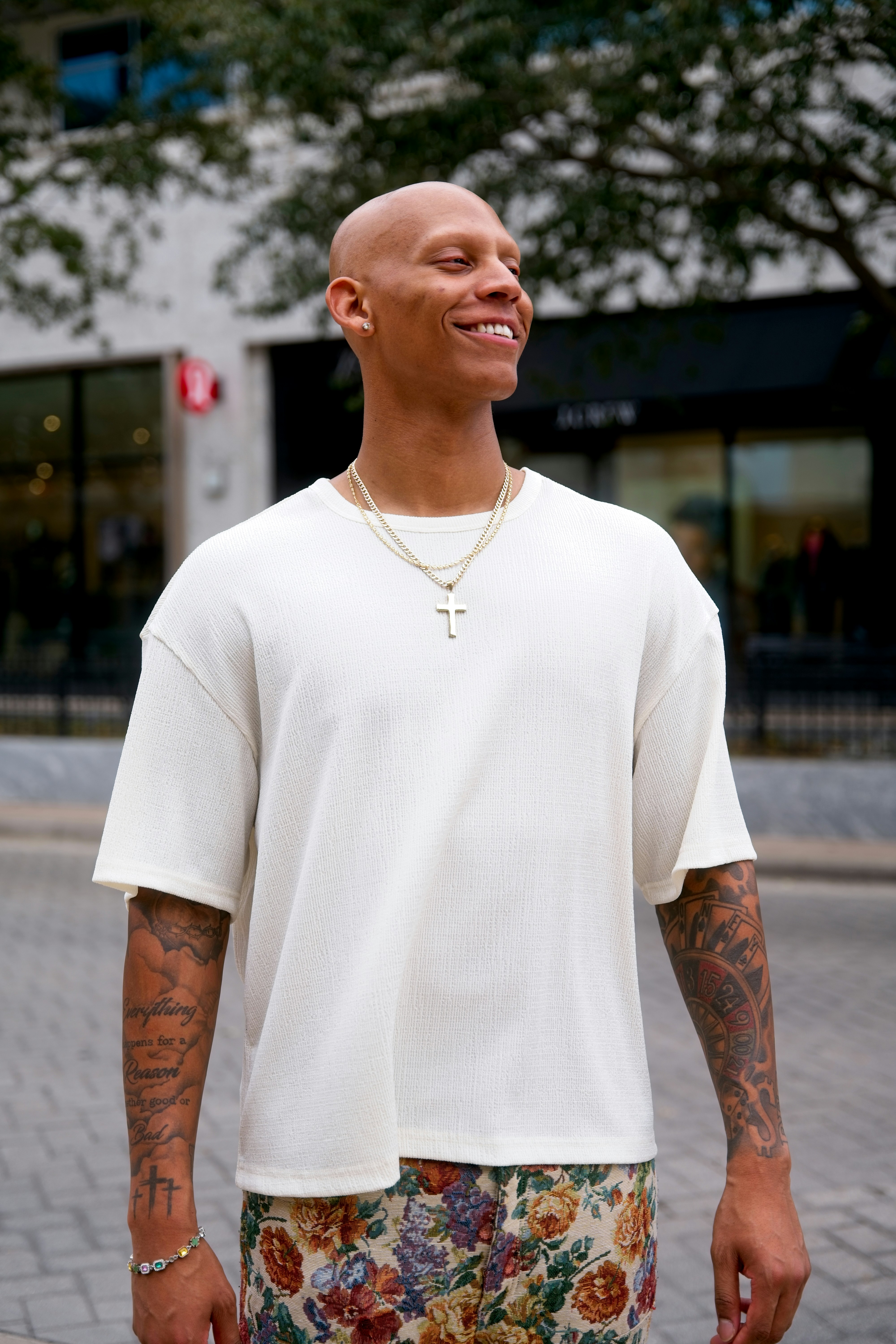 Homem careca de camisa branca e calça floral sorri