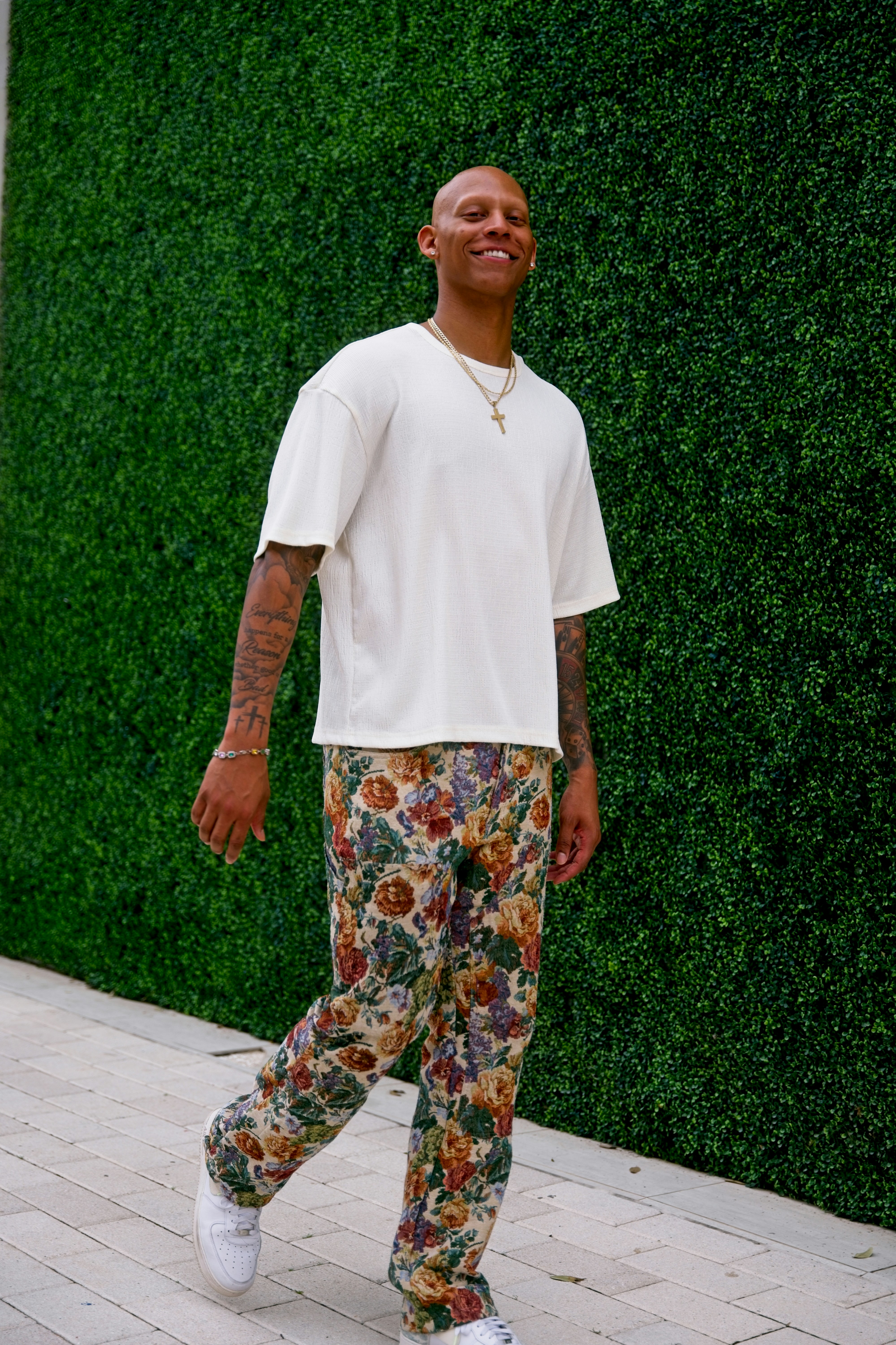 Um homem sorridente caminha em frente a um muro verde.