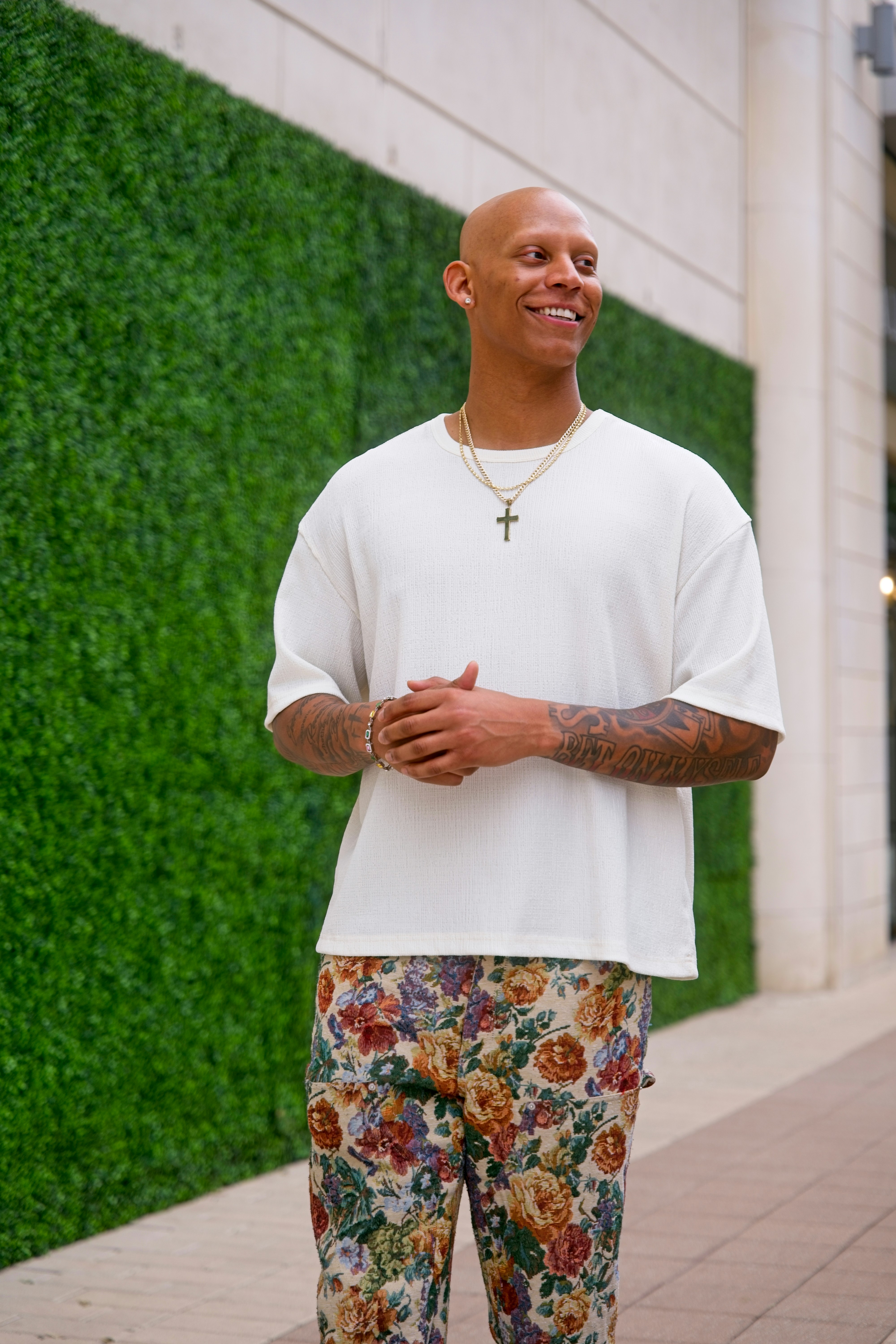 Homem careca de camisa branca e calça floral sorri.