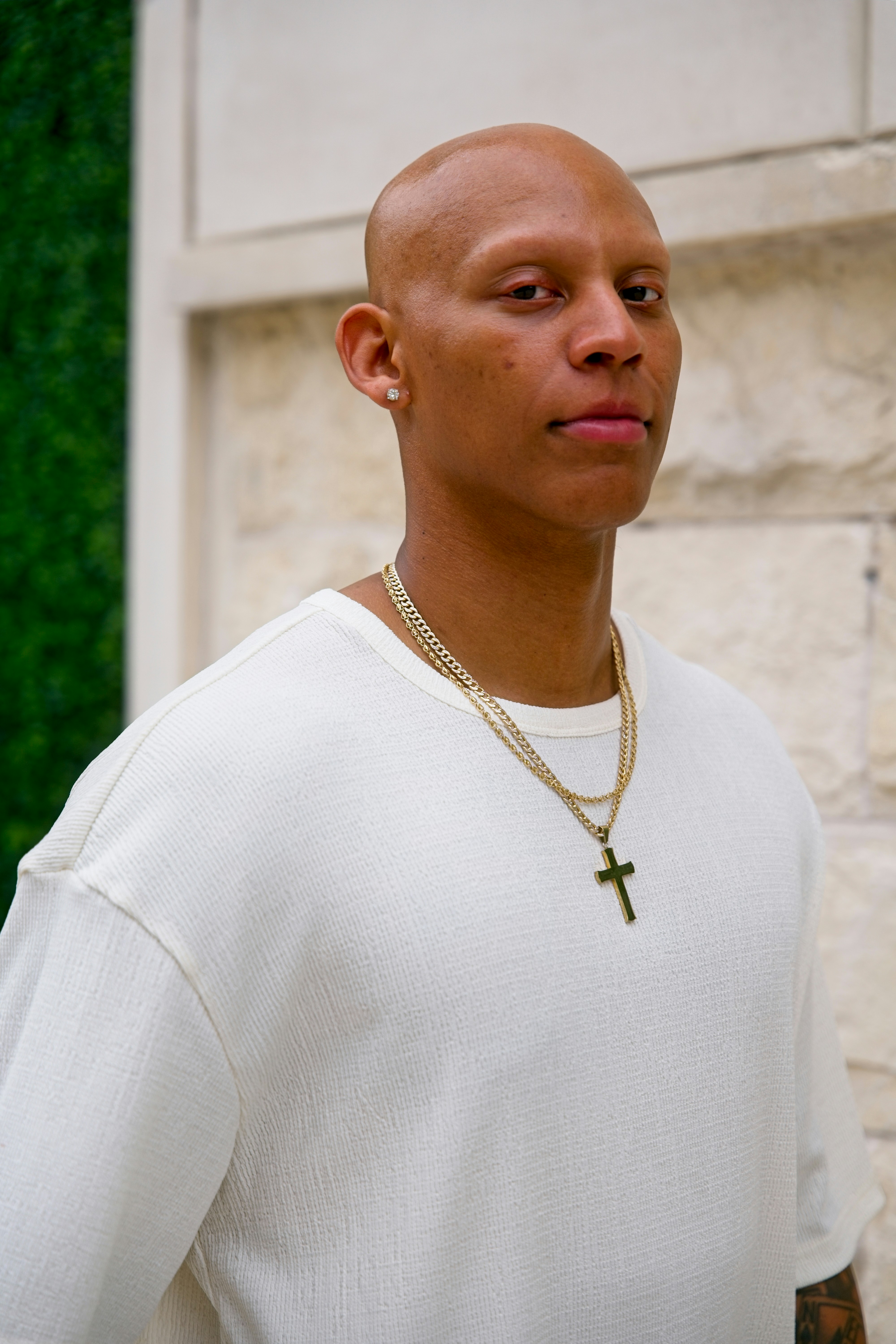 Um homem careca vestindo uma camiseta branca e colares dourados.